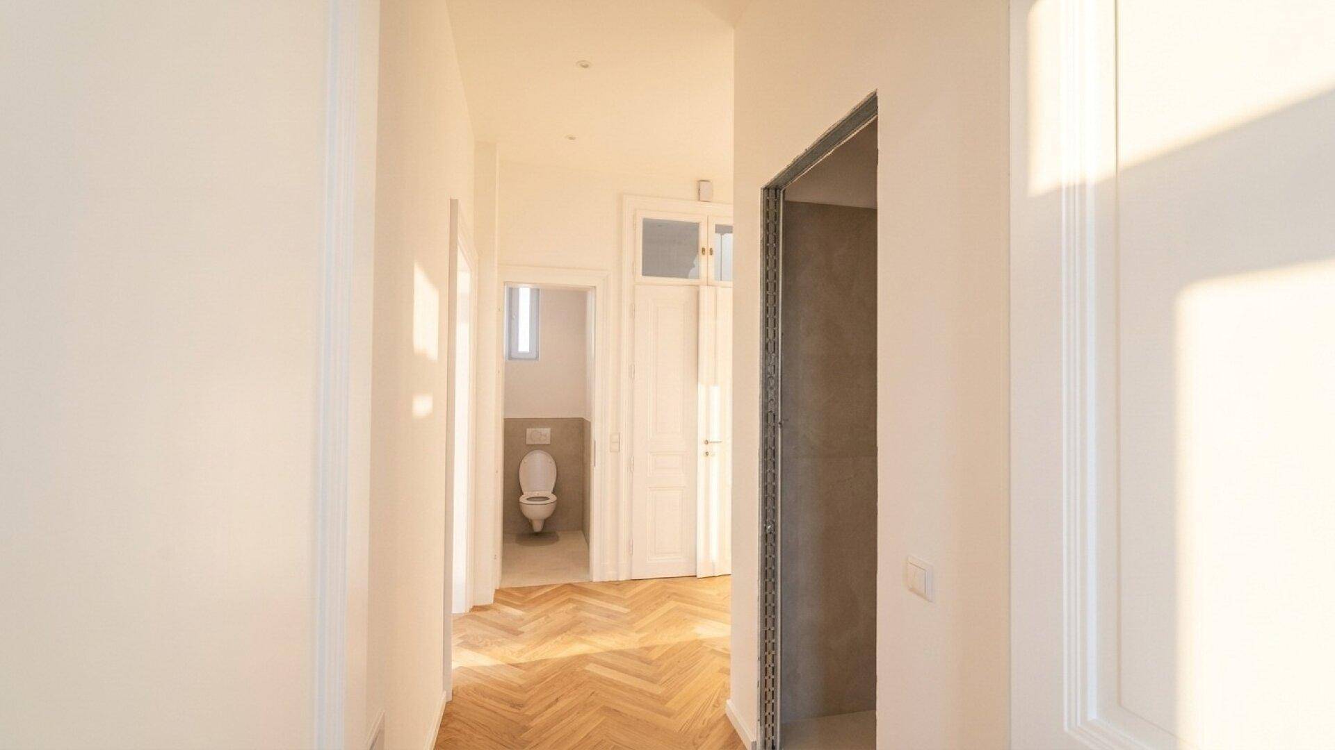 Heller Flur mit Fischgrätparkett, der zu einem separaten WC mit Fenster führt.