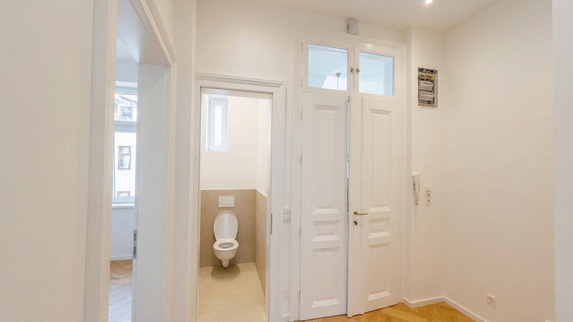 Heller Flur mit weißen Türen, der zu einem separaten WC mit Fenster führt.