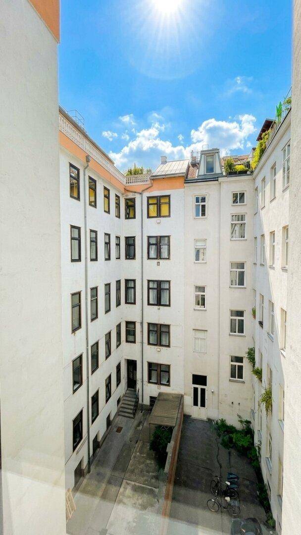 Sonniger Blick in einen ruhigen Innenhof mit weißen Fassaden und zahlreichen Fenstern.