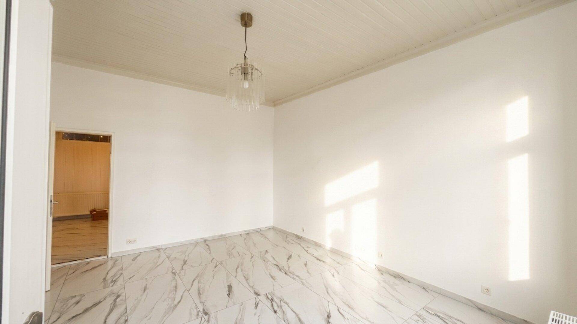 Heller Raum mit weißen Wänden, gemusterten Marmorfliesen und einem eleganten Kronleuchter an der Decke.