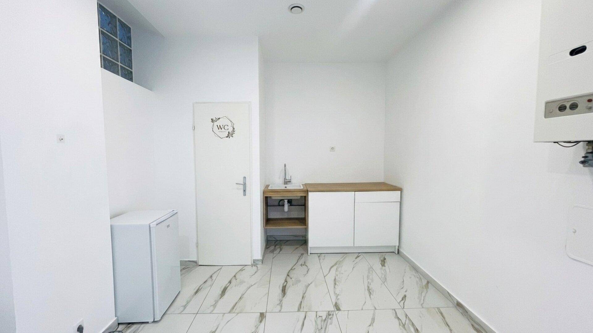 Bereich mit kleiner Küchenzeile, Spüle, Kühlschrank und einer Tür, die zu einer Toilette führt.