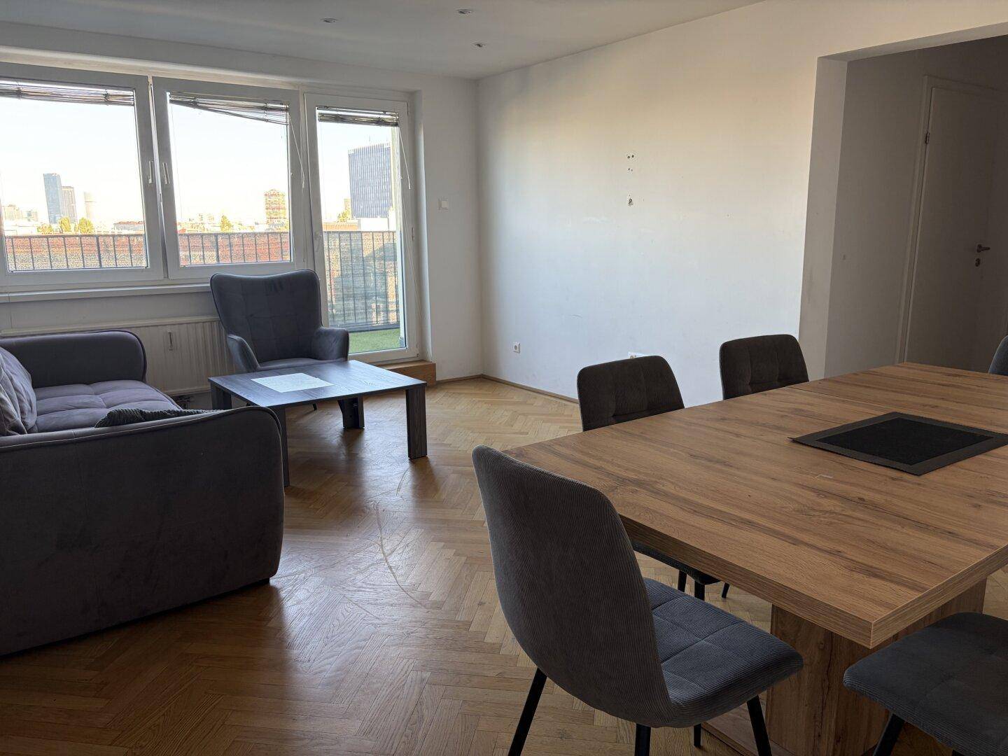 Geräumiger Wohnbereich mit großen Fenstern, die viel Tageslicht hereinlassen und Stadtblick bieten.