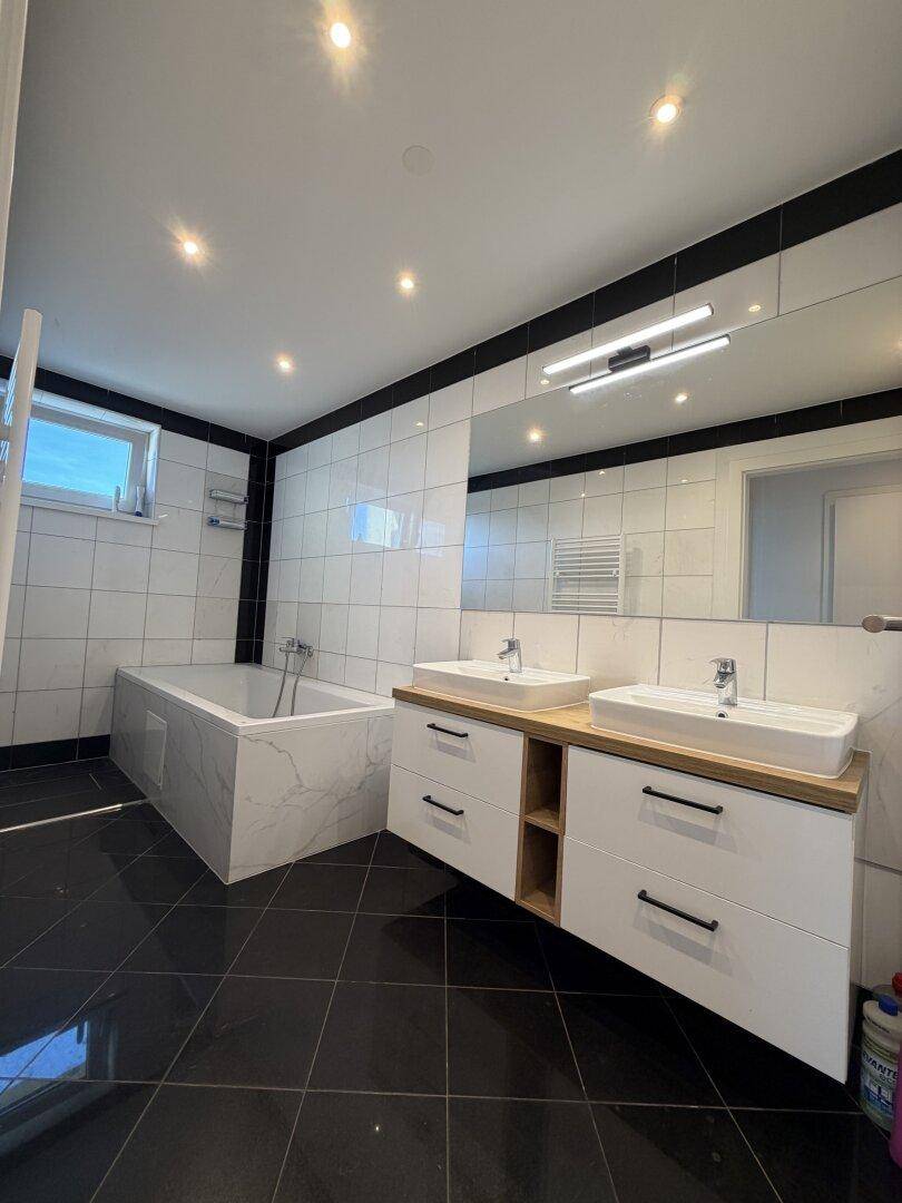 Modernes Badezimmer mit schwarz-weißen Fliesen, Badewanne und Doppelwaschbecken mit großem Spiegel.