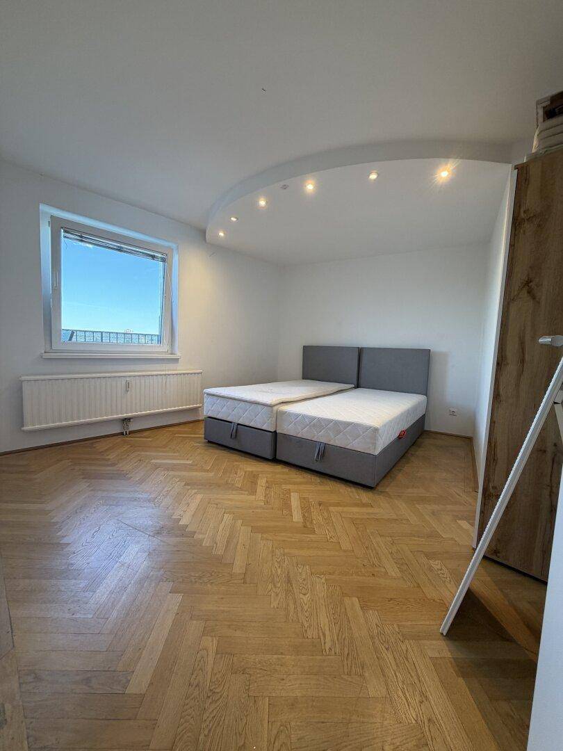 Helles Schlafzimmer mit Fischgrätparkett, Doppelbett und einem Fenster, das viel Licht spendet.