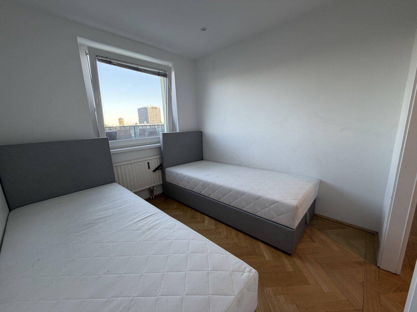 Zweites Schlafzimmer mit zwei Einzelbetten, Parkettboden und einem Fenster mit Stadtblick.