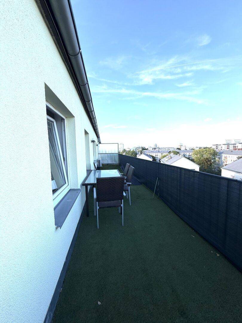 Langer Balkon mit Kunstrasen, Esstisch und Stühlen, ideal für Mahlzeiten im Freien mit Stadtblick.