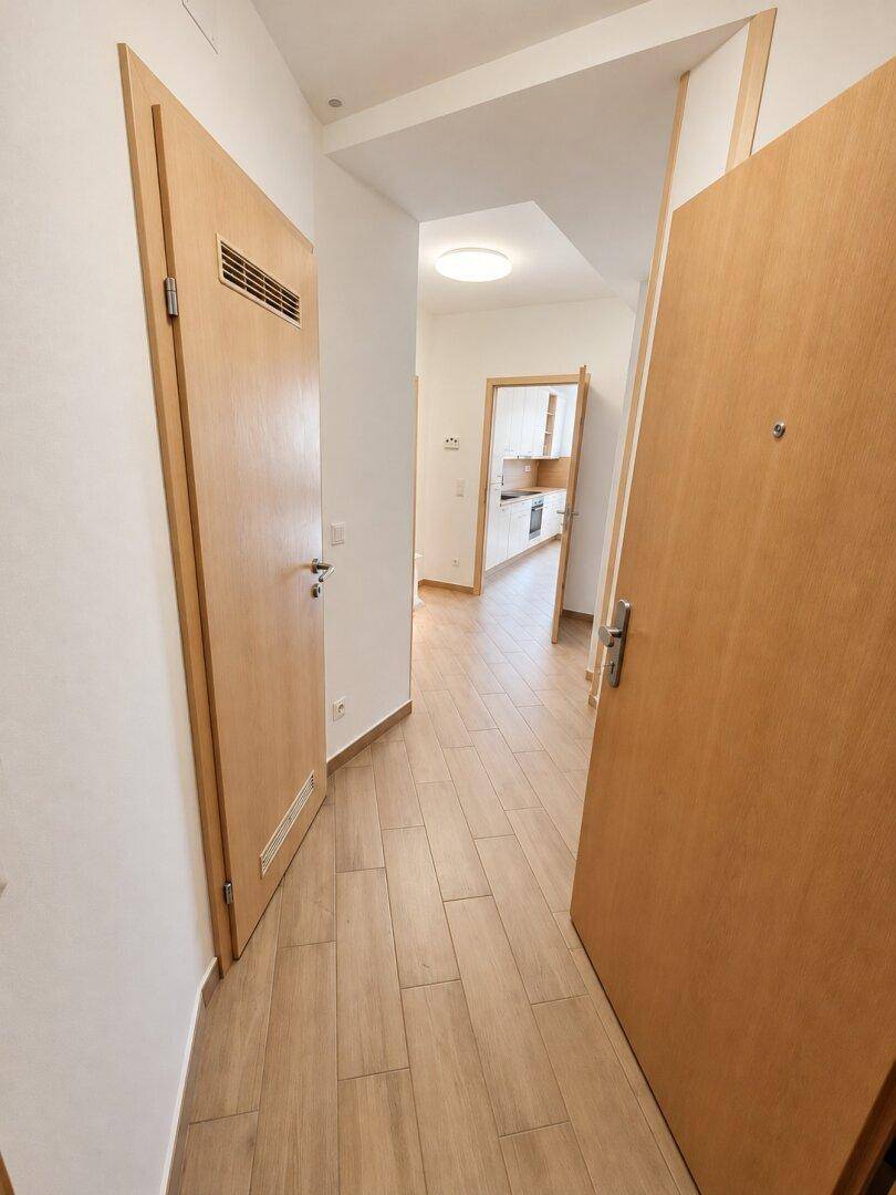 Heller Flur mit Holztüren und Fliesenboden, der zu weiteren Räumen führt.