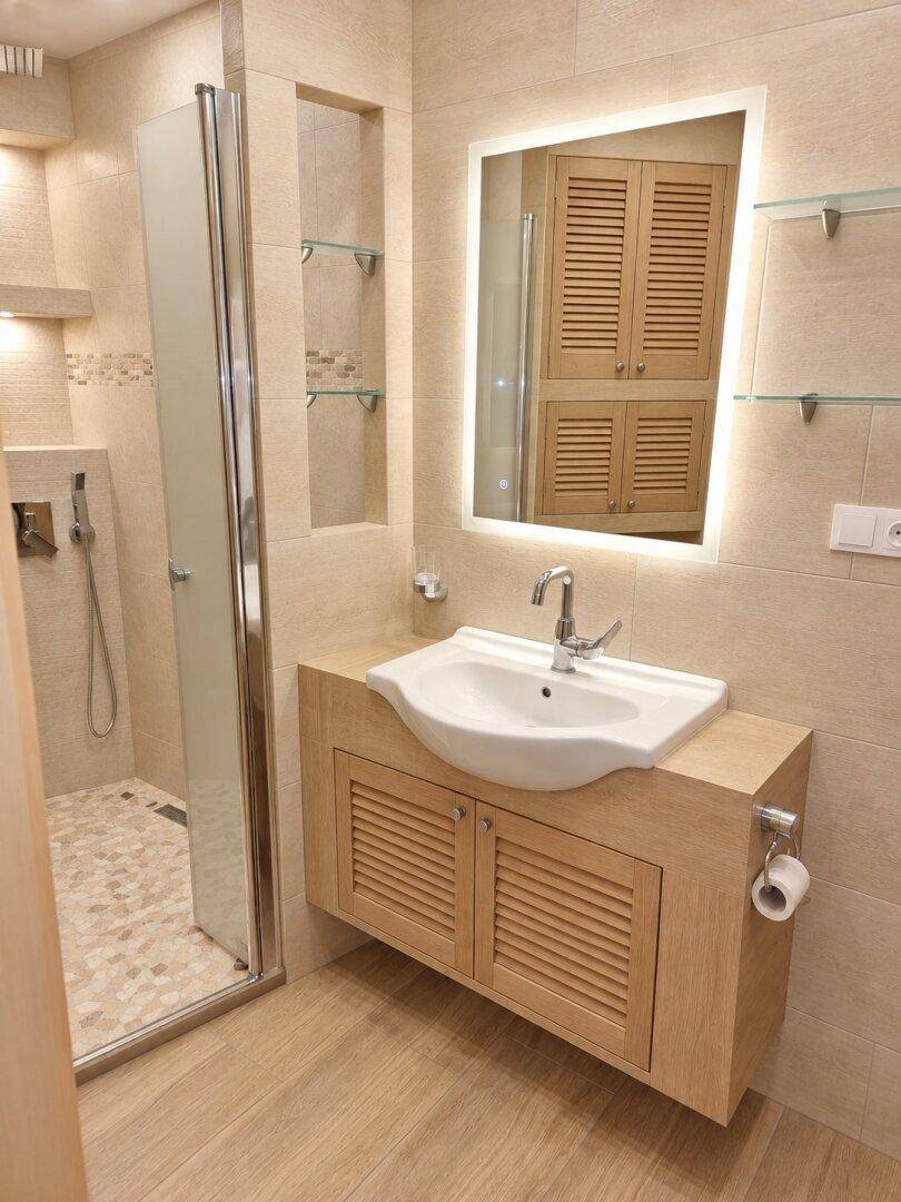 Modernes Badezimmer mit Waschtisch, beleuchtetem Spiegel und Duschkabine.