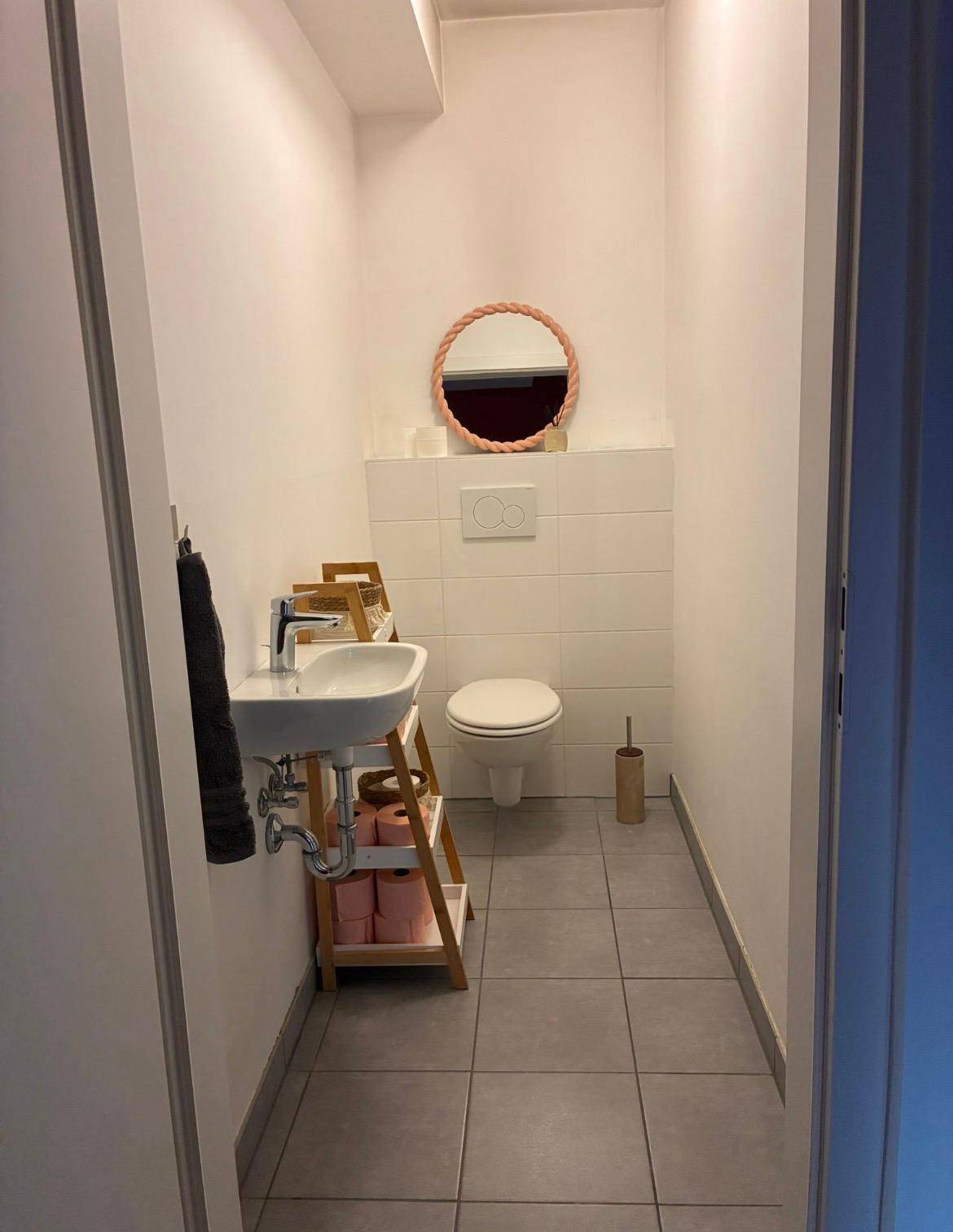 Kleines Gäste-WC mit Toilette, Handwaschbecken und modernen grauen Bodenfliesen, schlicht eingerichtet.
