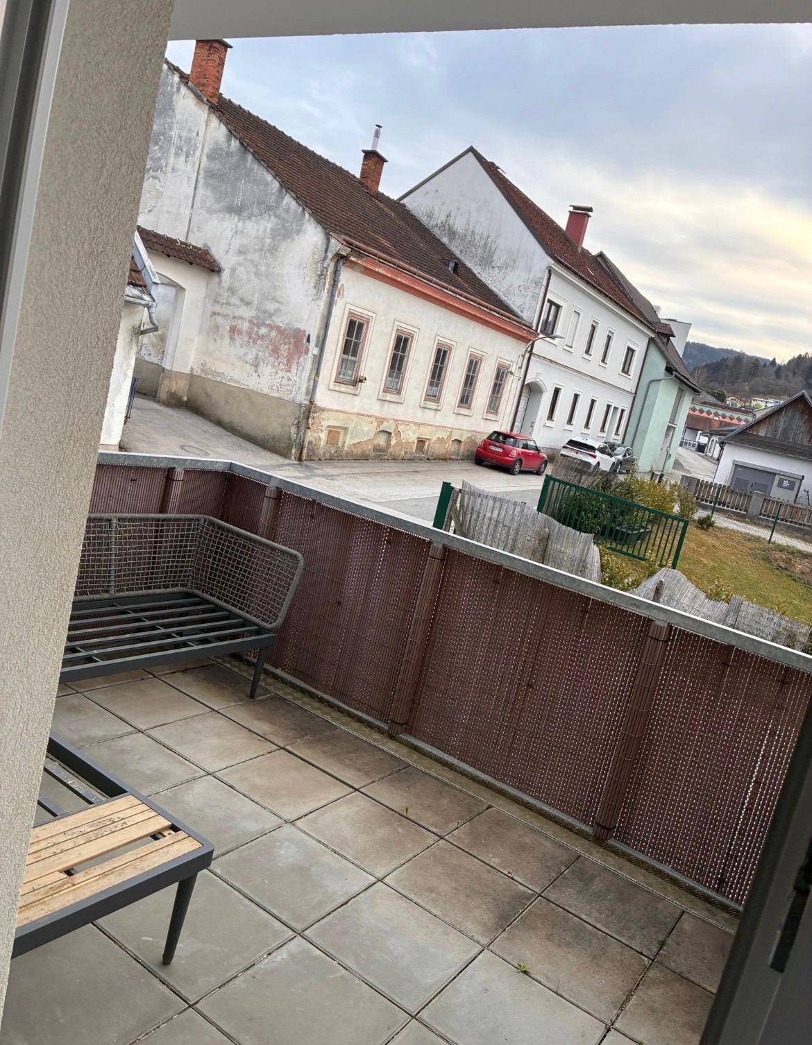 Balkon mit Fliesenboden und Blick auf eine Straße mit historischen Gebäuden und grüne Hügel.