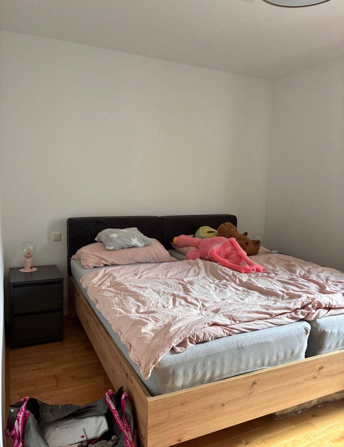 Helles Schlafzimmer mit Doppelbett, Nachttisch und warmem Holzboden, einfach und funktional eingerichtet.