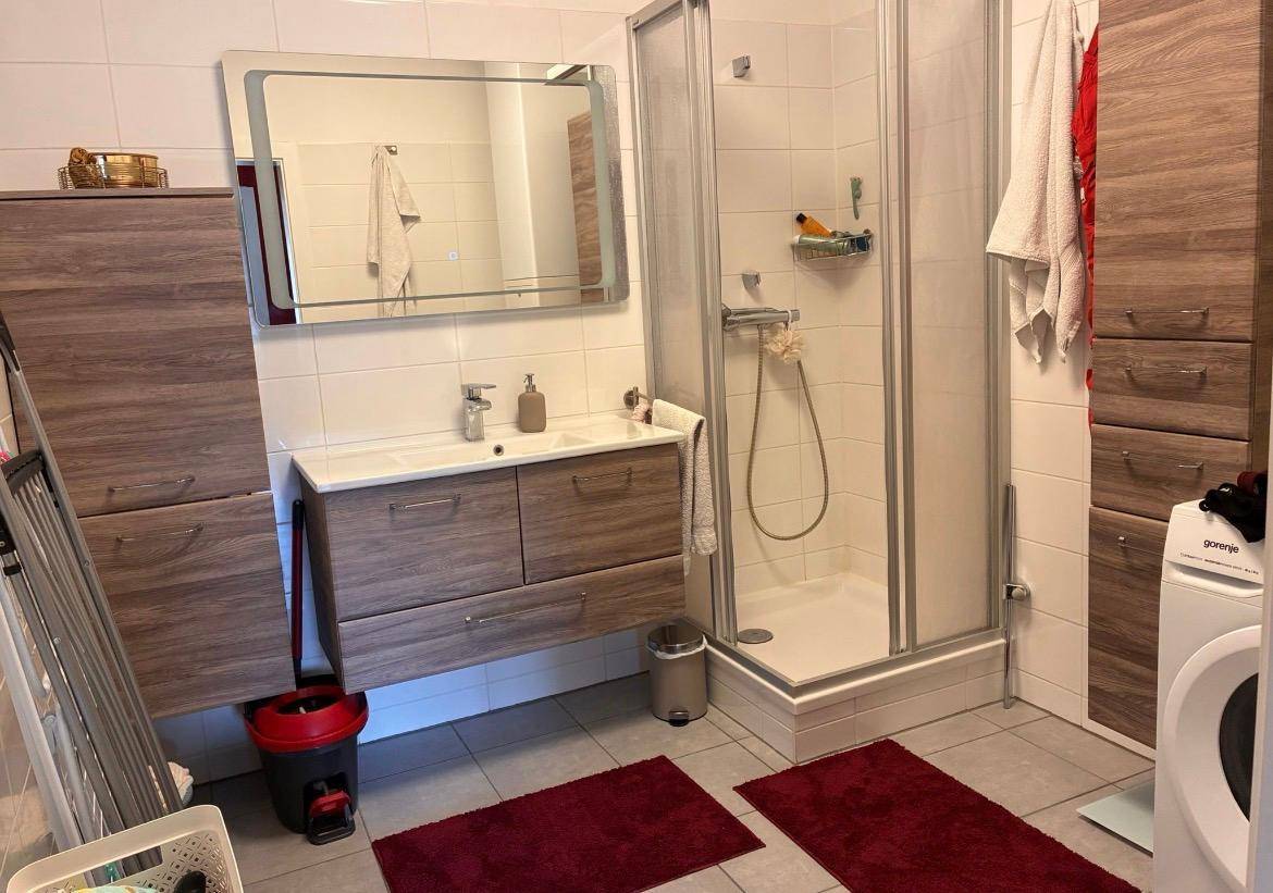 Modernes Badezimmer mit Duschkabine, Doppelwaschbecken und Waschmaschine, ausgestattet mit hellen Fliesen.