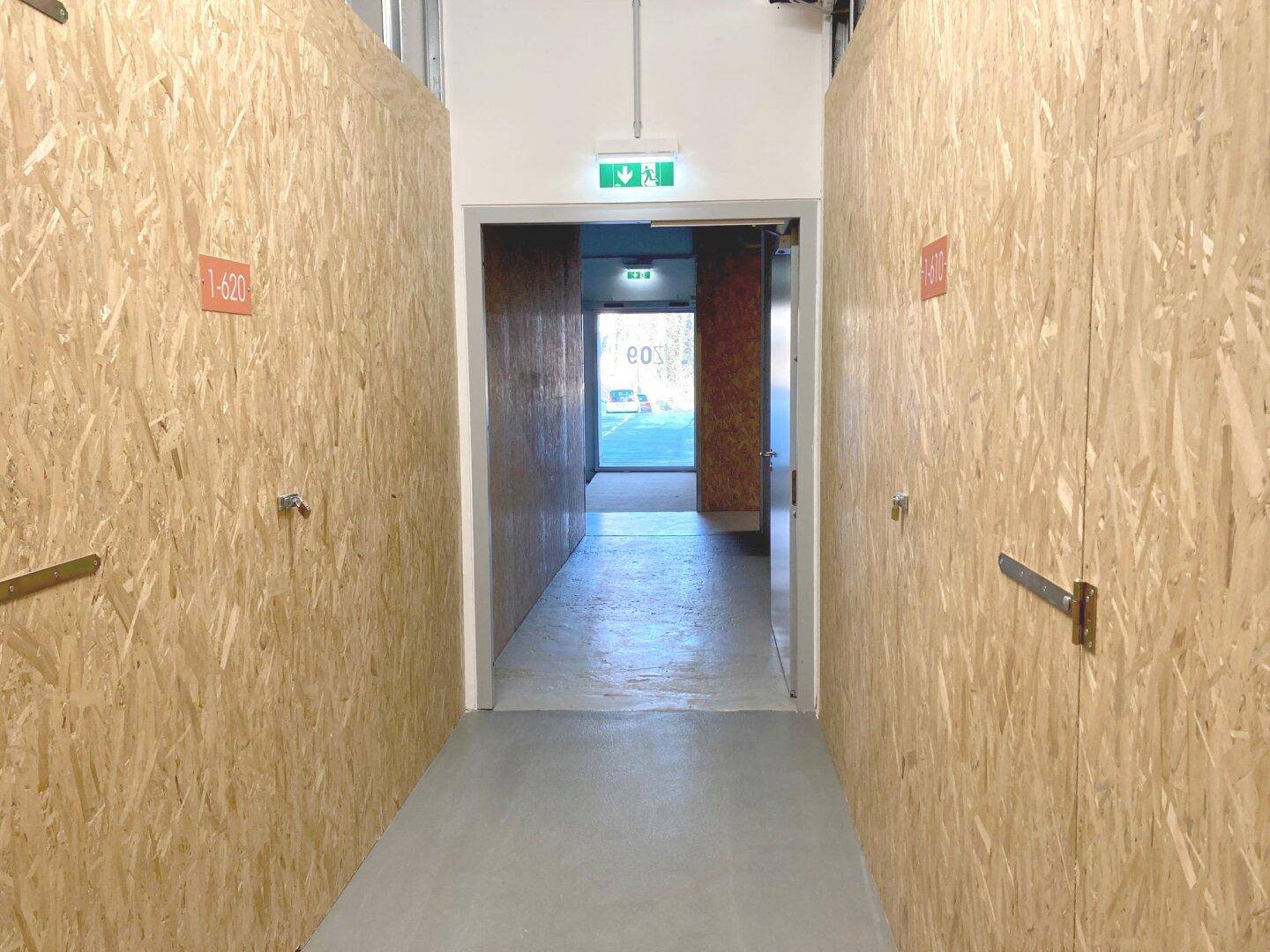 Langer Flur mit individuellen Lagereinheiten aus OSB-Platten und einem Ausgangsschild.