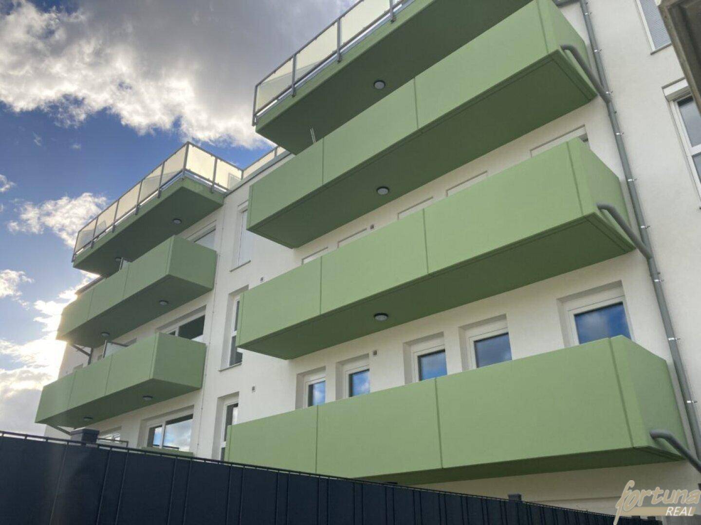 Fassade des modernen Gebäudes mit markanten grünen Balkonen unter blauem Himmel.