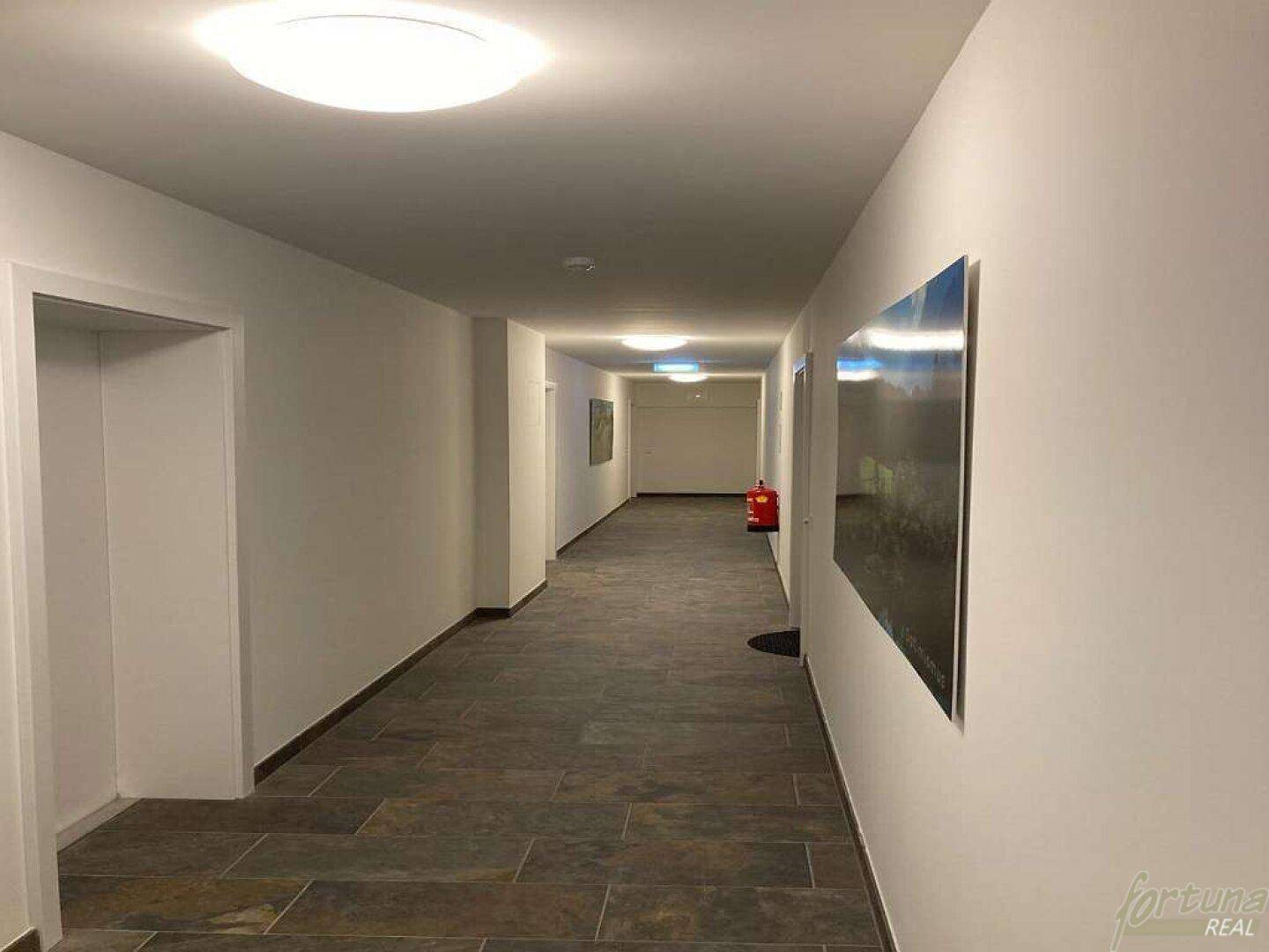 Heller und langer Flur im Gemeinschaftsbereich mit Fliesenboden und moderner Beleuchtung.