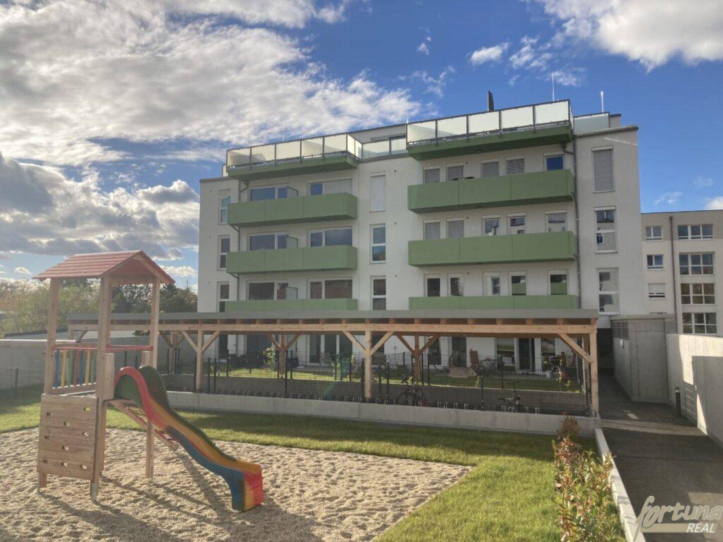 Modernes Wohngebäude mit Spielplatz und überdachtem Bereich im Außenbereich.
