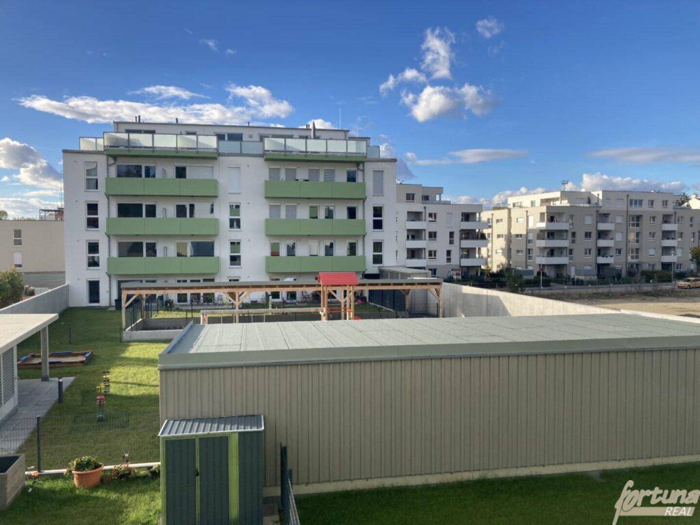 Neubaukomplex mit grünen Balkonen und einem Gemeinschaftsgarten im Hintergrund.