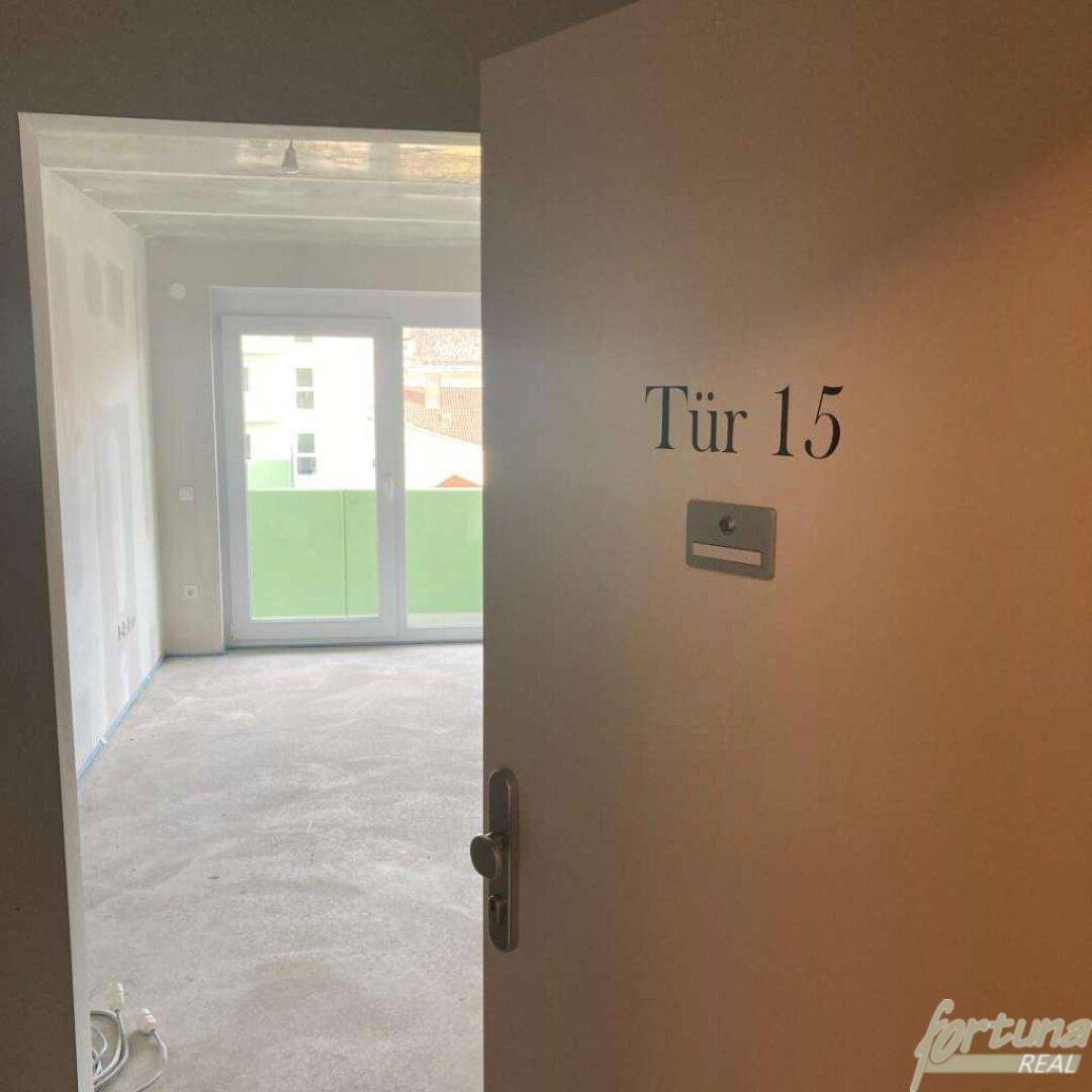 Blick durch eine offene Tür mit der Nummer 15 in einen unfertigen Raum mit Balkonzugang.