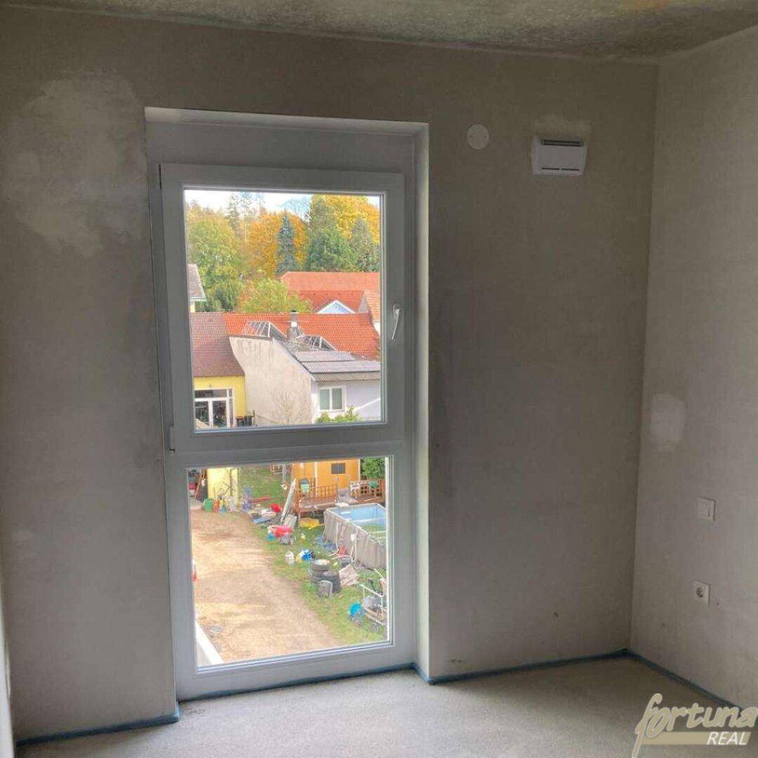 Unfertiger Raum mit Fensterblick auf eine Wohnsiedlung und einen Aufstellpool im Garten.