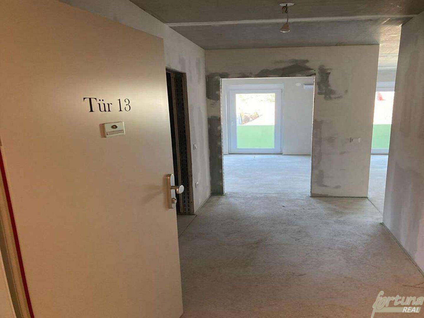 Eingangsbereich mit Tür Nummer 13 und Blick in den unfertigen Flur der Wohnung.