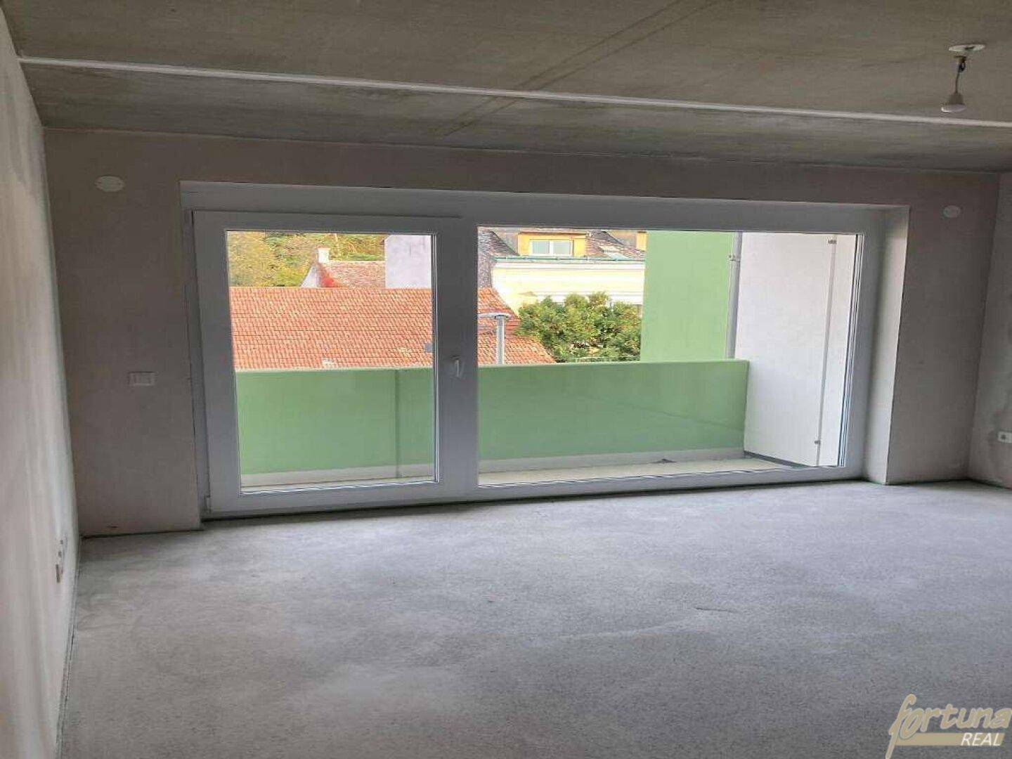 Unfertiger Wohnbereich mit großem Schiebefenster und Zugang zum Balkon.