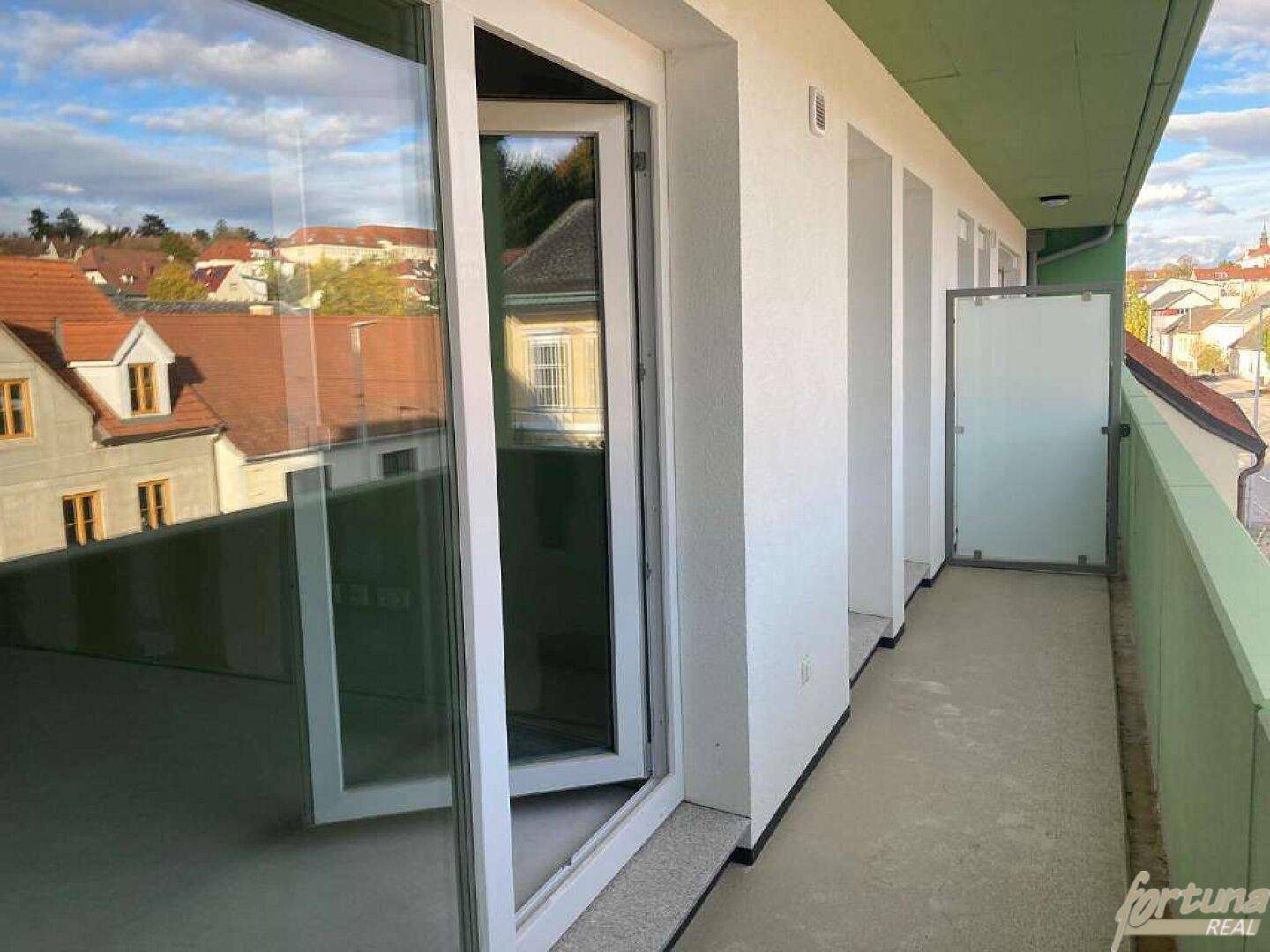 Langer Balkon mit Glasbrüstung und Blick auf die umliegenden Dächer und Gebäude der Stadt.