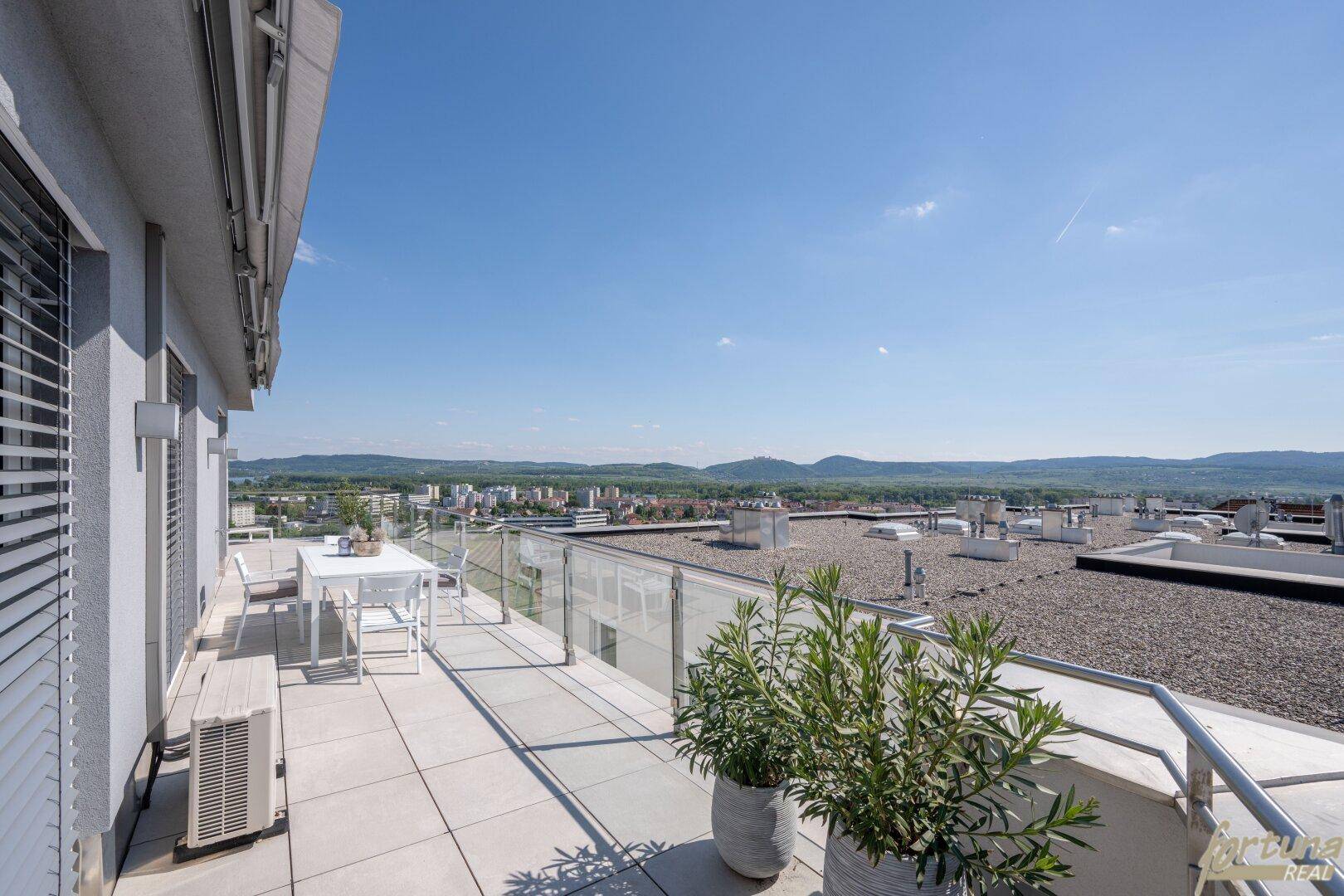 Sonniger Terrassenbereich mit Sitzgelegenheiten und Panoramablick über die Dächer und die Umgebung.