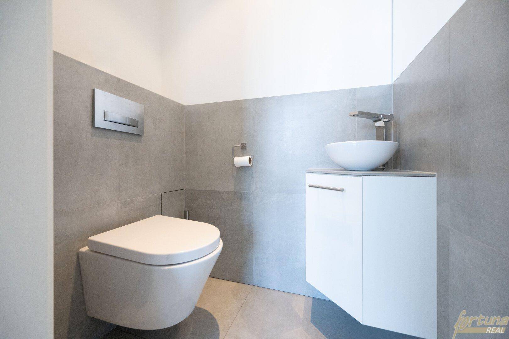 Helles Gäste-WC mit modernem Wand-WC, kleinem Waschbecken und stilvollen grauen Fliesen.