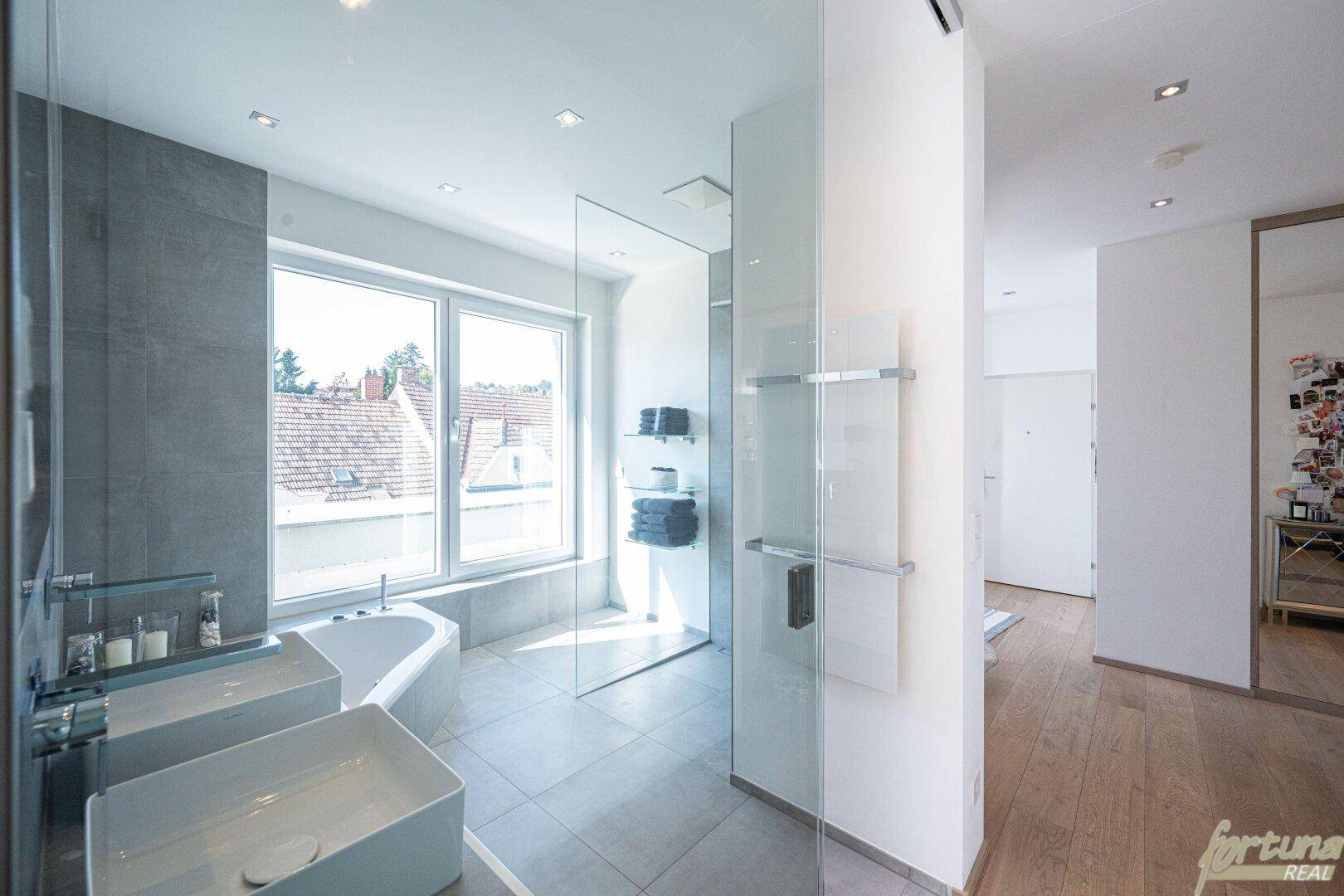 Modernes Badezimmer mit Doppelwaschbecken, Badewanne, begehbarer Dusche und großem Fenster.