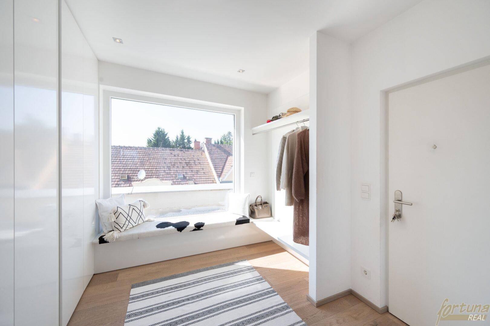 Heller Eingangsbereich mit Fensterbank als Sitzgelegenheit, Garderobe und Holzboden.