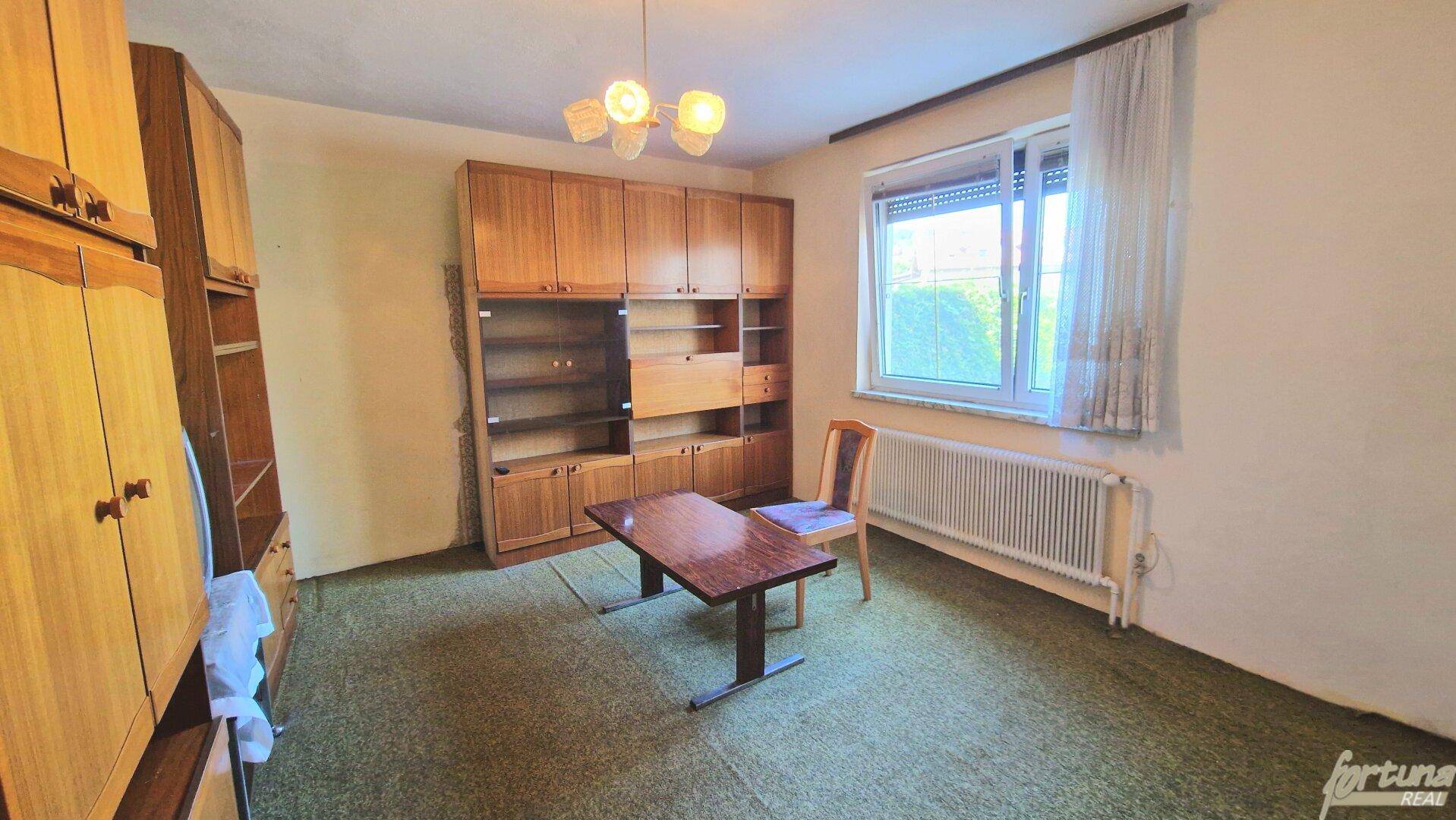 Geräumiges Zimmer mit grünem Teppichboden und großem Holzschrank, einfach eingerichtet.