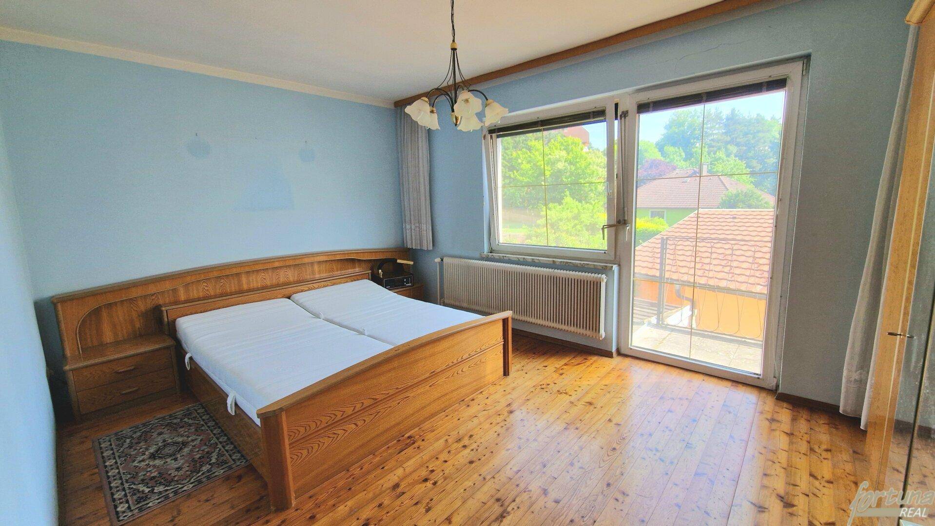 Helles Schlafzimmer mit Holzbett, blauen Wänden und Parkettboden, mit Zugang zum Balkon.