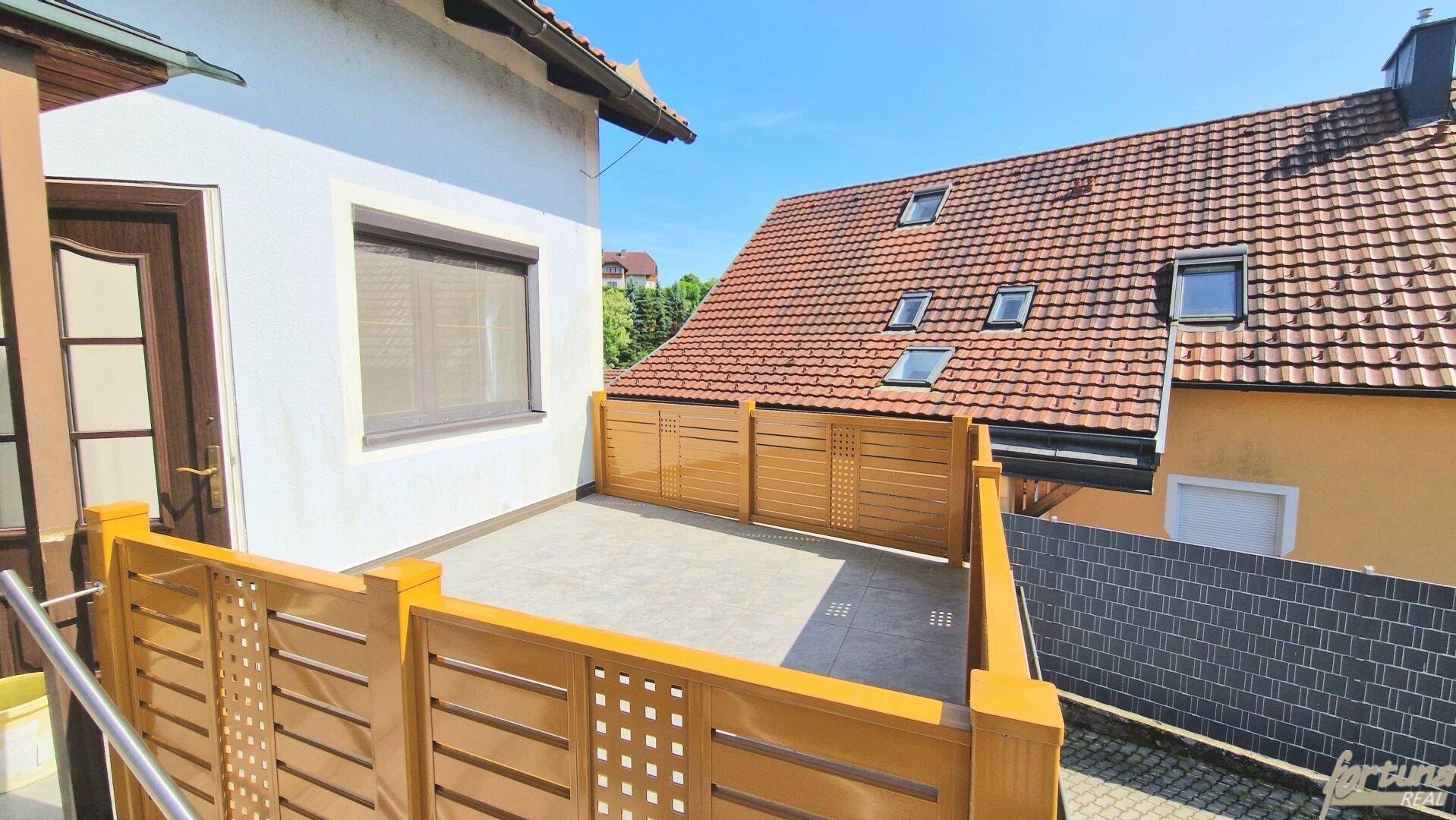 Geräumige Terrasse mit Holzzaun und Blick auf das Nachbardach mit Dachfenstern.