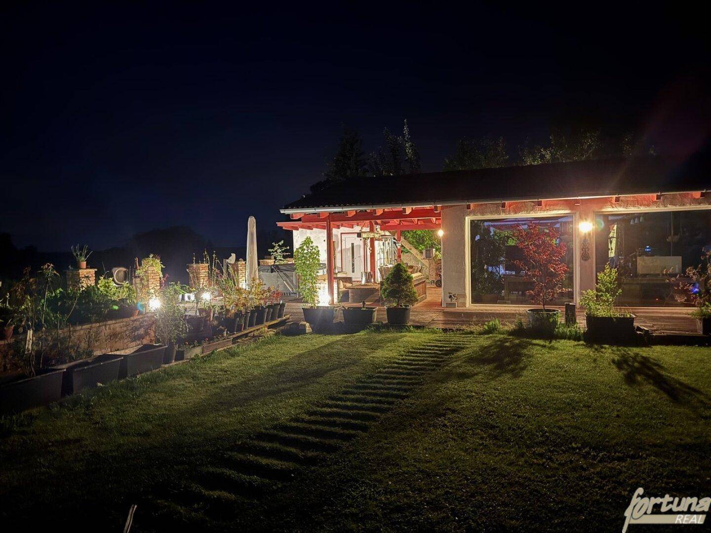 Garten und Hausfassade bei Nacht, stimmungsvoll beleuchtet mit Wegen und Pflanzen.