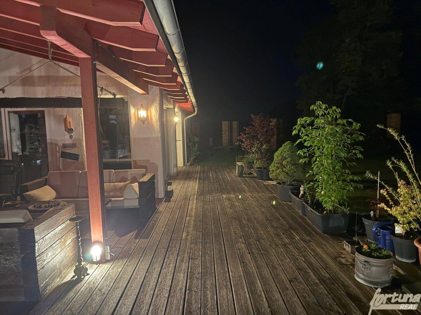 Beleuchtete Holzterrasse bei Nacht mit Pflanzen und gemütlicher Atmosphäre.