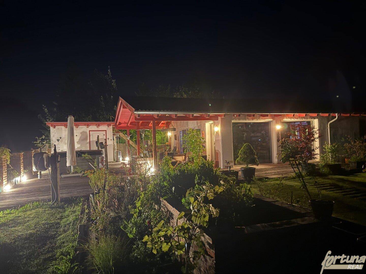 Nächtliche Ansicht des Gartens und der Terrasse mit indirekter Beleuchtung und Pflanzen.