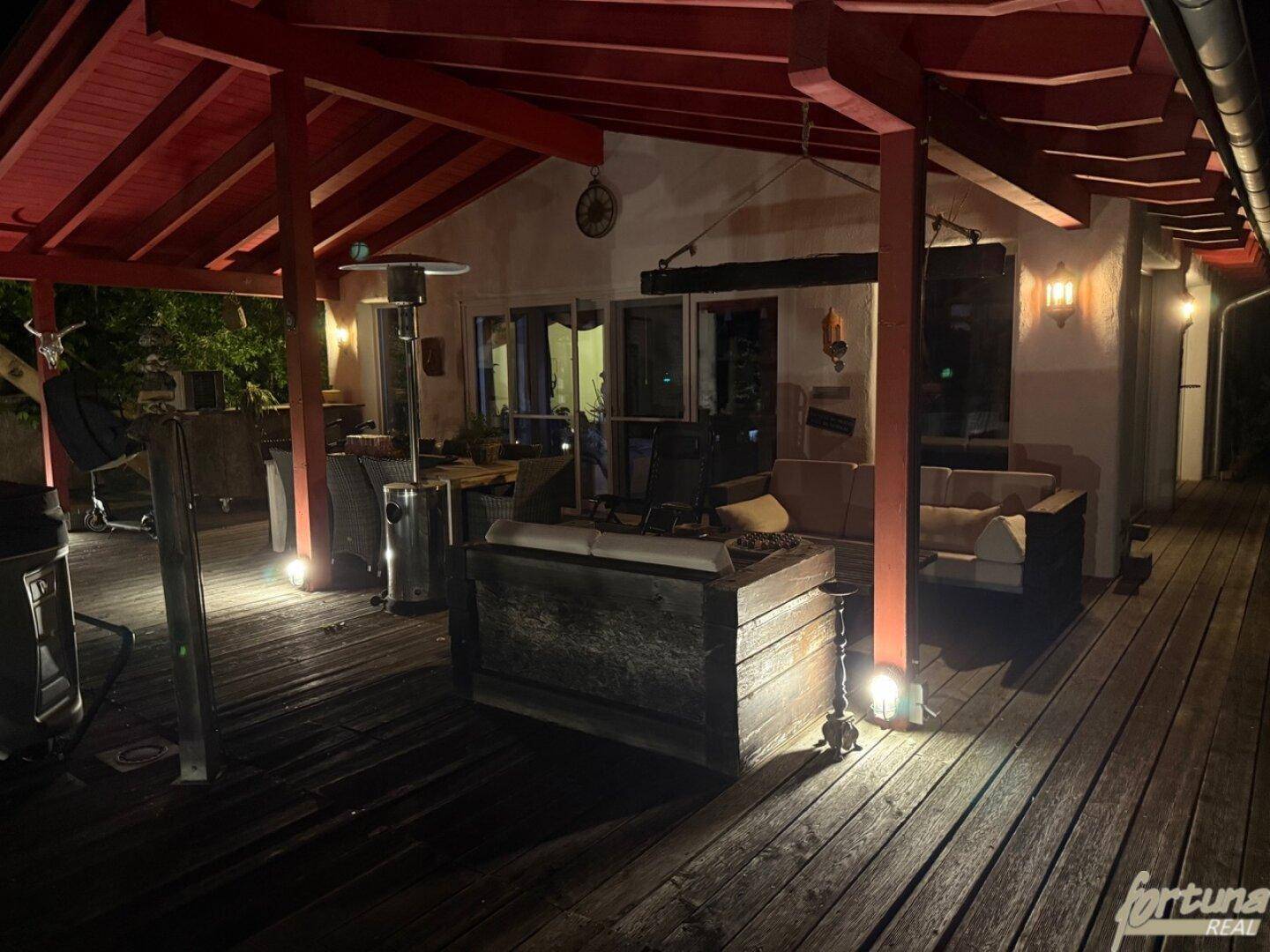 Gemütliche, beleuchtete Terrasse bei Nacht mit Sitzgelegenheiten und einem Heizstrahler.