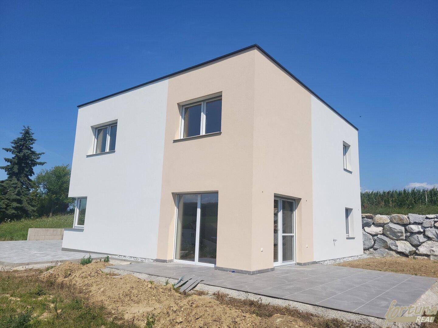 Rückansicht des modernen Hauses mit Terrassenzugang und angrenzender Steinmauer.