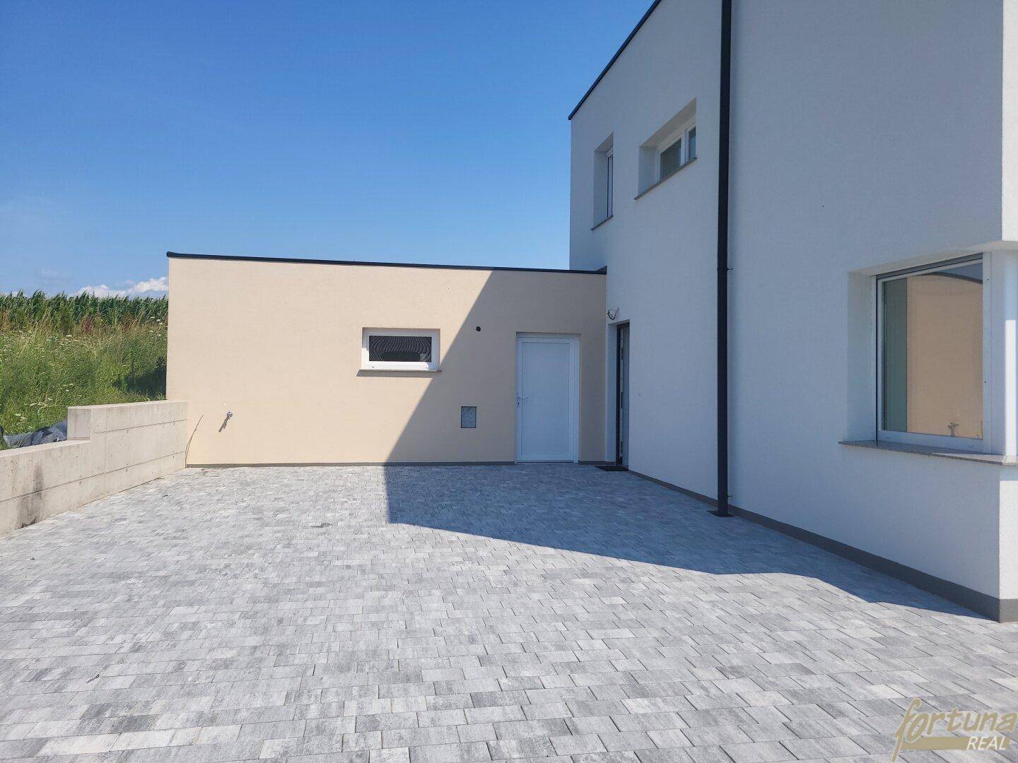 Gepflasterter Vorplatz und Seitenansicht des Hauses mit Eingangsbereich und kleinerem Anbau.