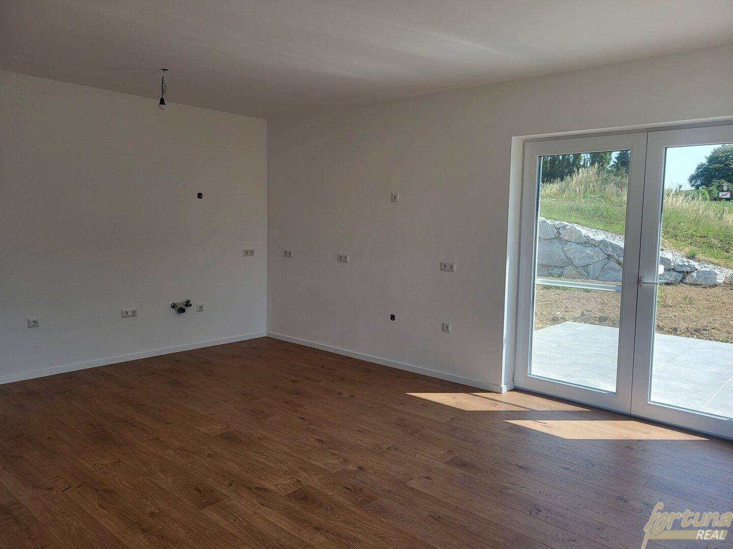 Heller Raum mit Holzboden und großer Schiebetür, die Zugang zum Außenbereich bietet.