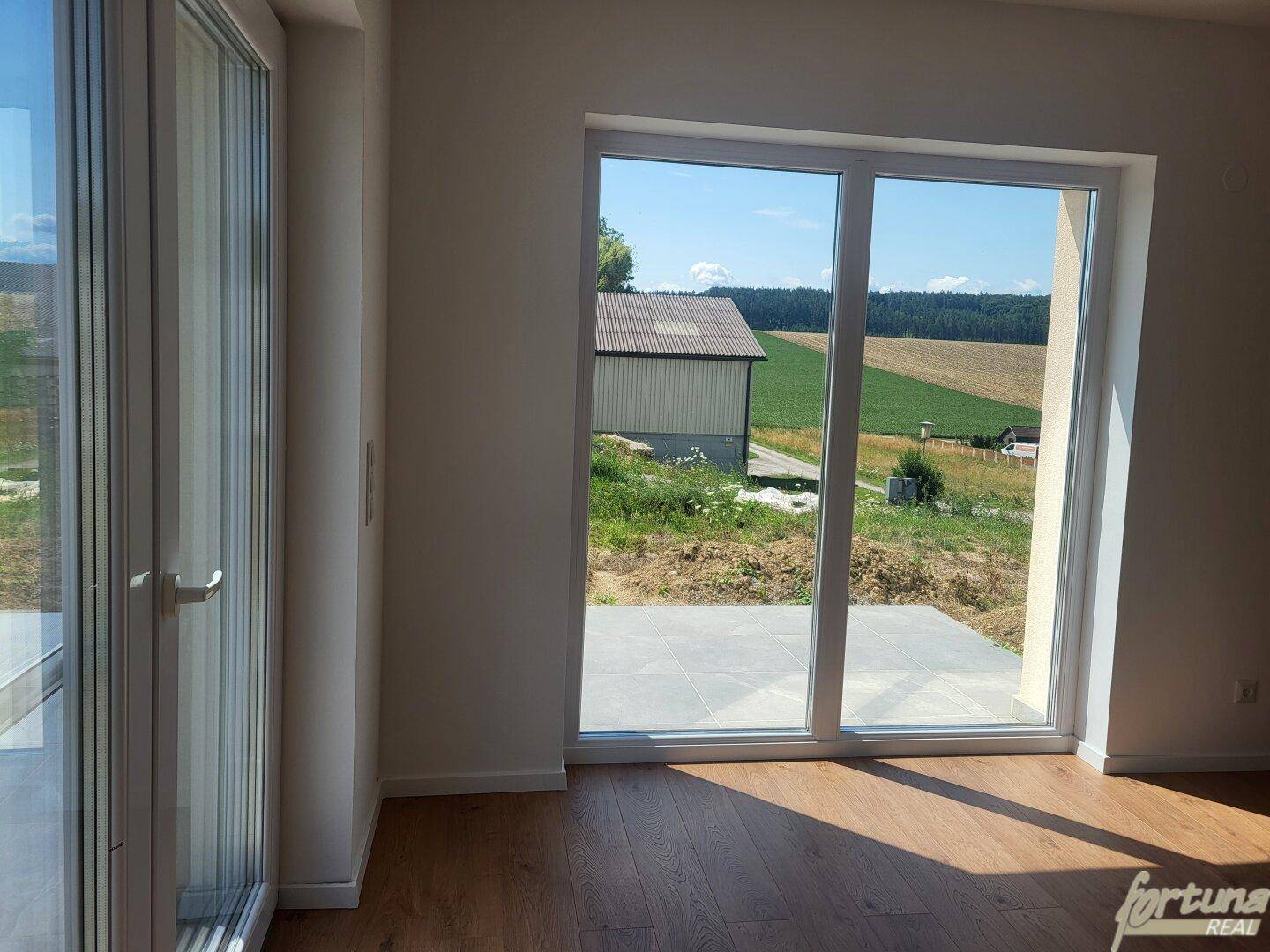 Große Fensterfront mit weitem Blick auf die ländliche Umgebung und angrenzende Gebäude.