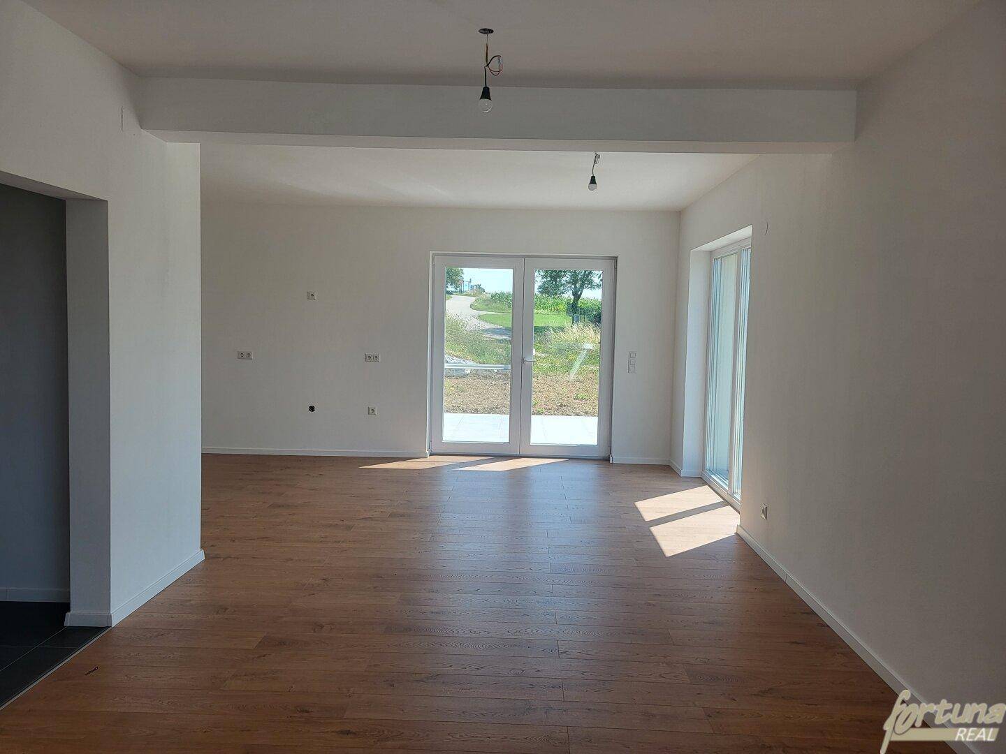 Geräumiges Wohnzimmer mit Holzboden und großen Fenstern, die viel Tageslicht hereinlassen.