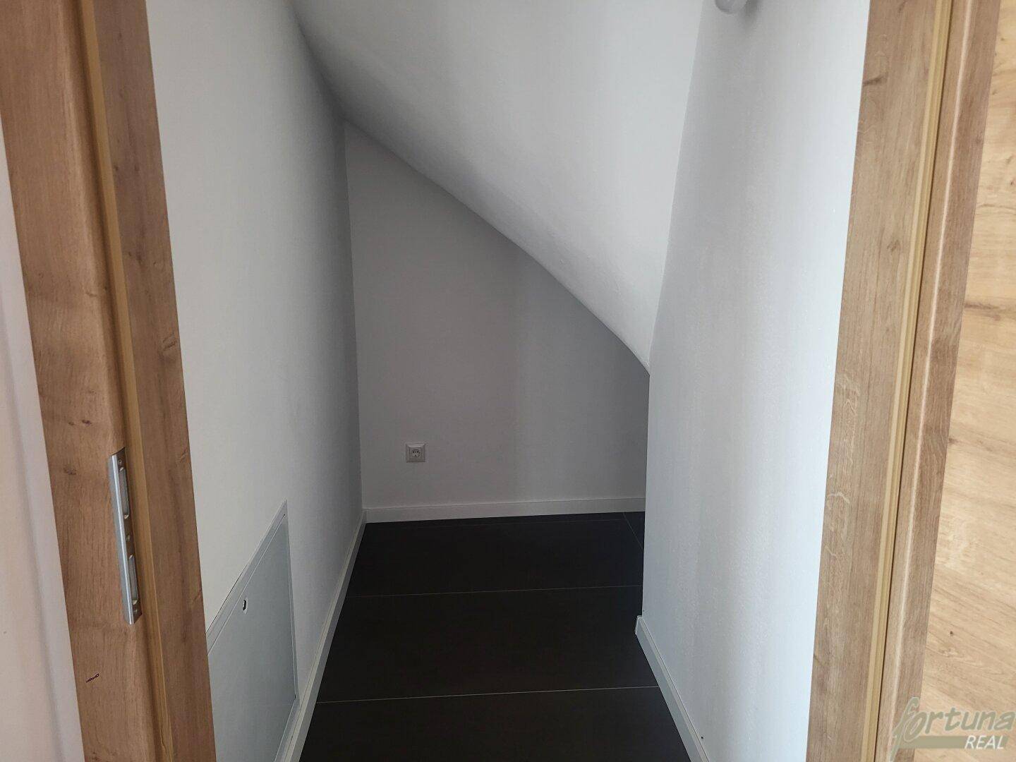 Praktischer Abstellraum unter der Dachschräge mit dunklem Fliesenboden.
