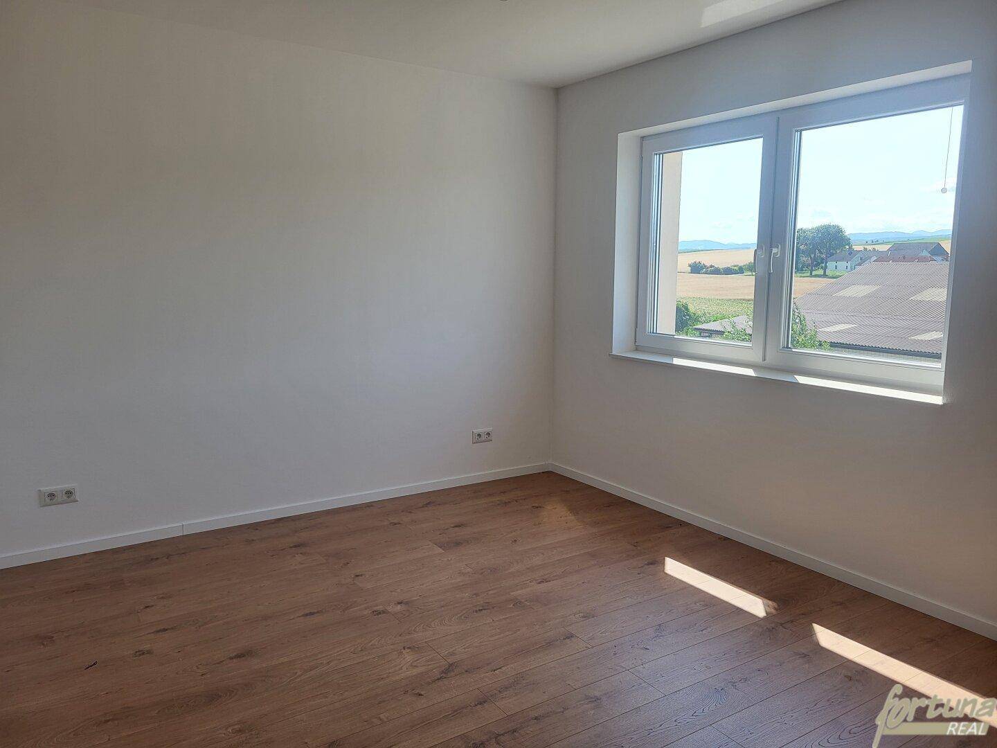 Helles Schlafzimmer mit Holzboden und Fenster, das viel Sonnenlicht hereinlässt.