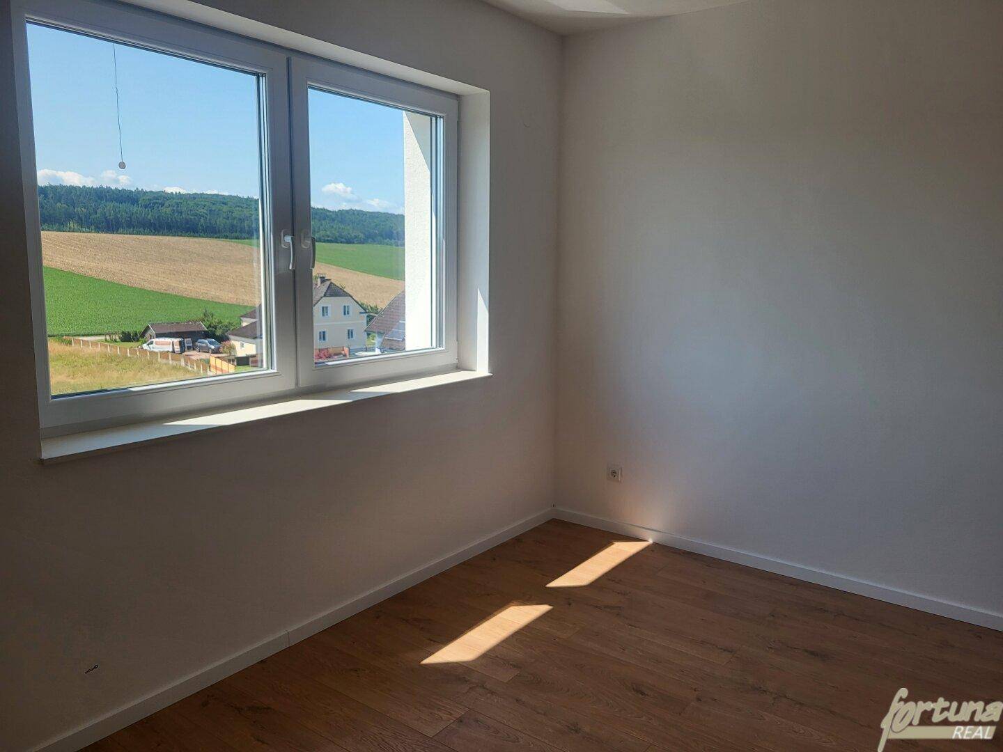 Schlafzimmer mit Holzboden und Fenster, das einen weiten Blick auf die Landschaft bietet.