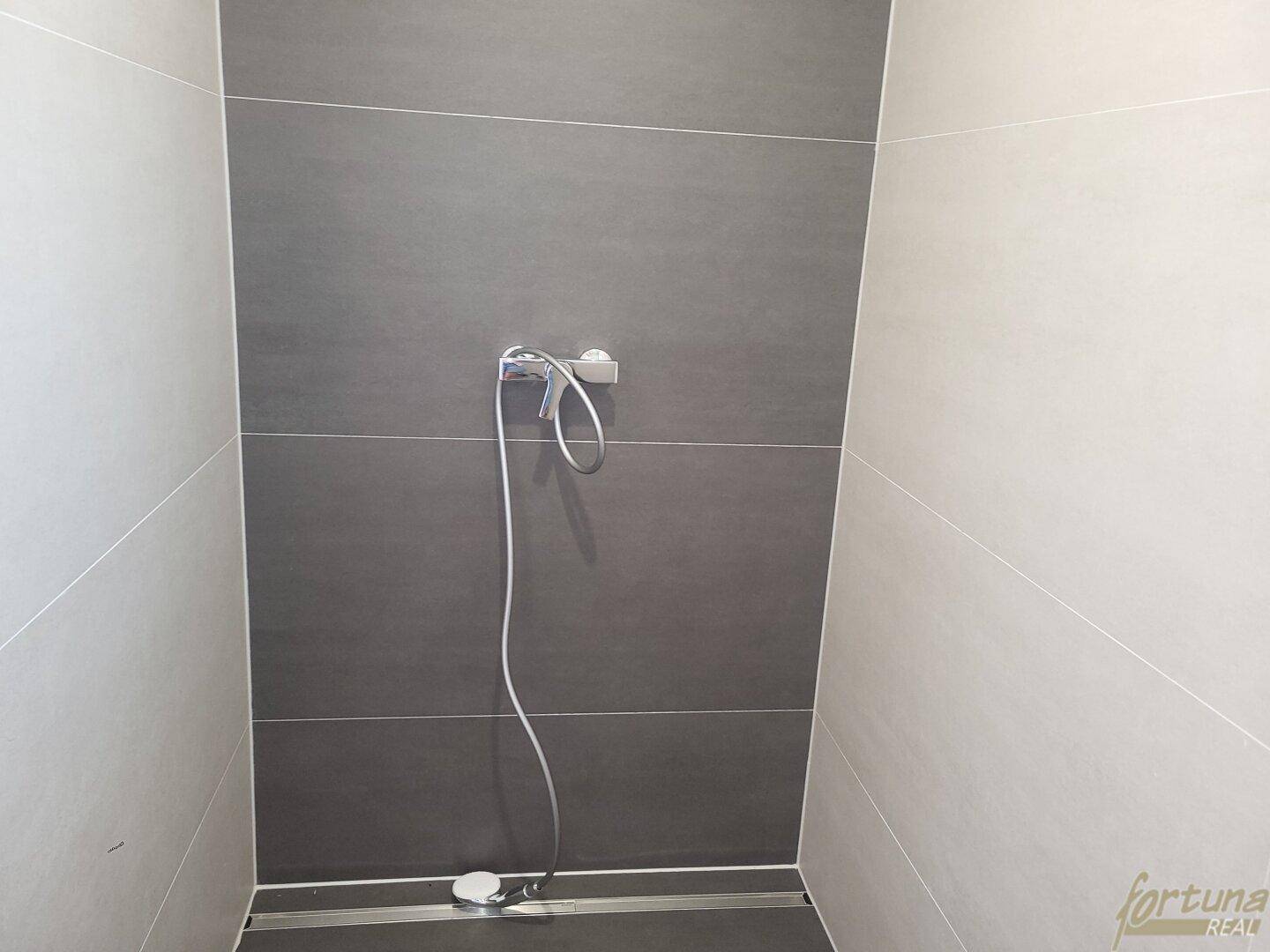 Moderne Duschkabine mit großformatigen grauen Fliesen und minimalistischer Armatur.