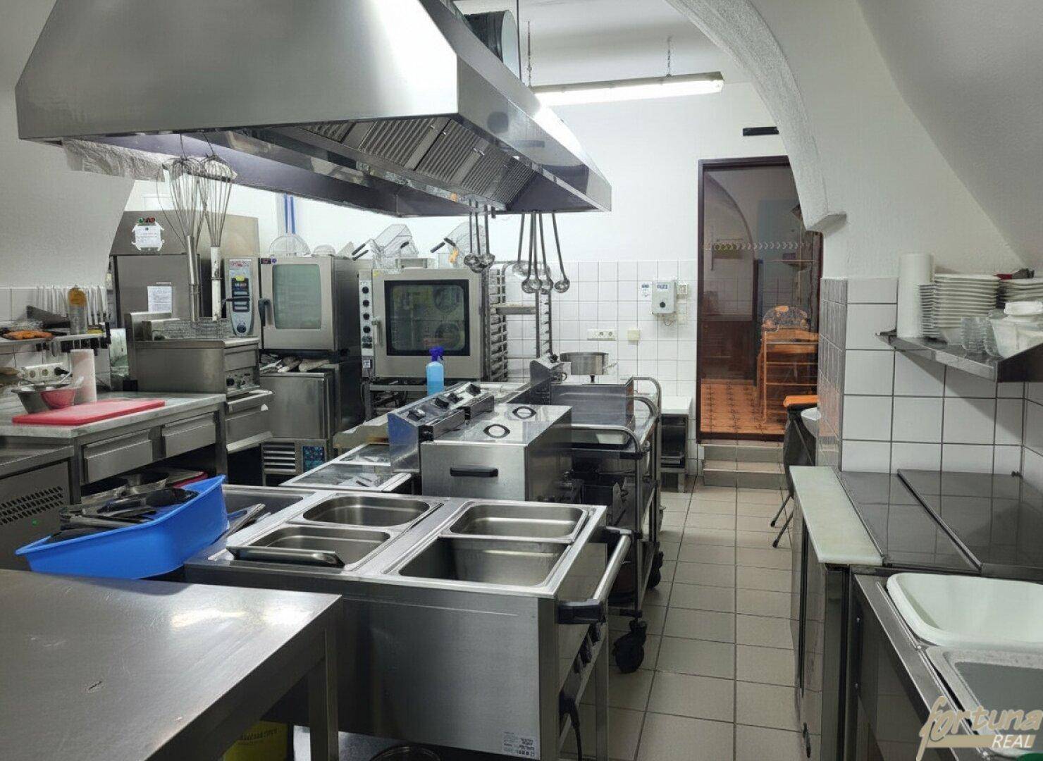 Professionelle Großküche mit Edelstahlgeräten, Fliesenboden und einem leistungsstarken Abluftsystem für den Gastronomiebetrieb.