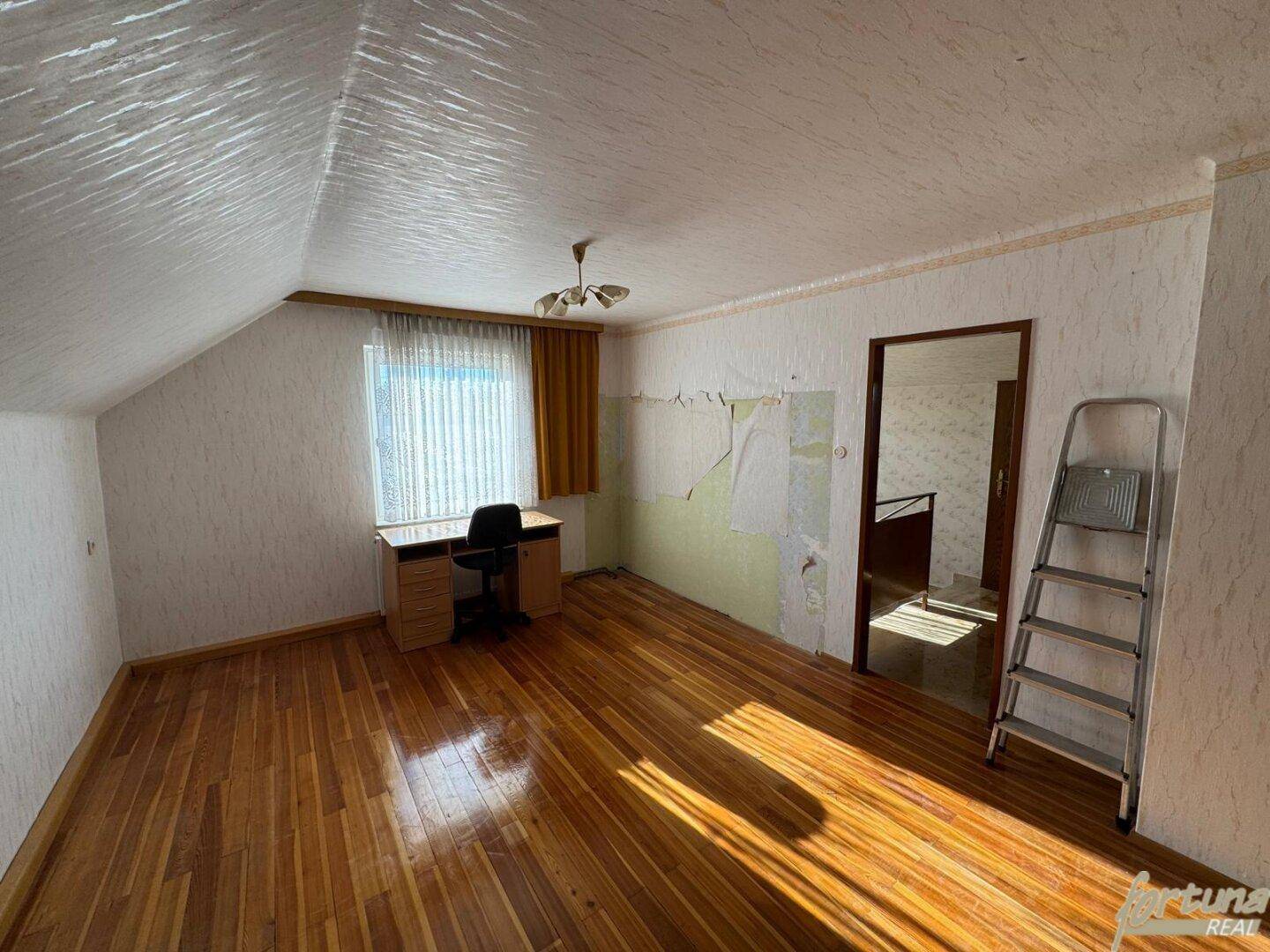 Zimmer im Dachgeschoss mit Holzboden, Schreibtisch und teilweise entfernter Tapete.