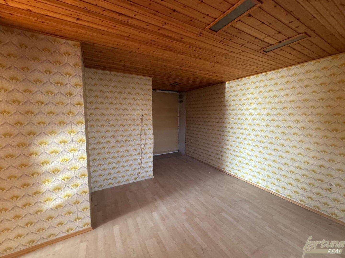 Leerer Raum mit Holzdecke und gemusterter Tapete, bereit für individuelle Gestaltung.