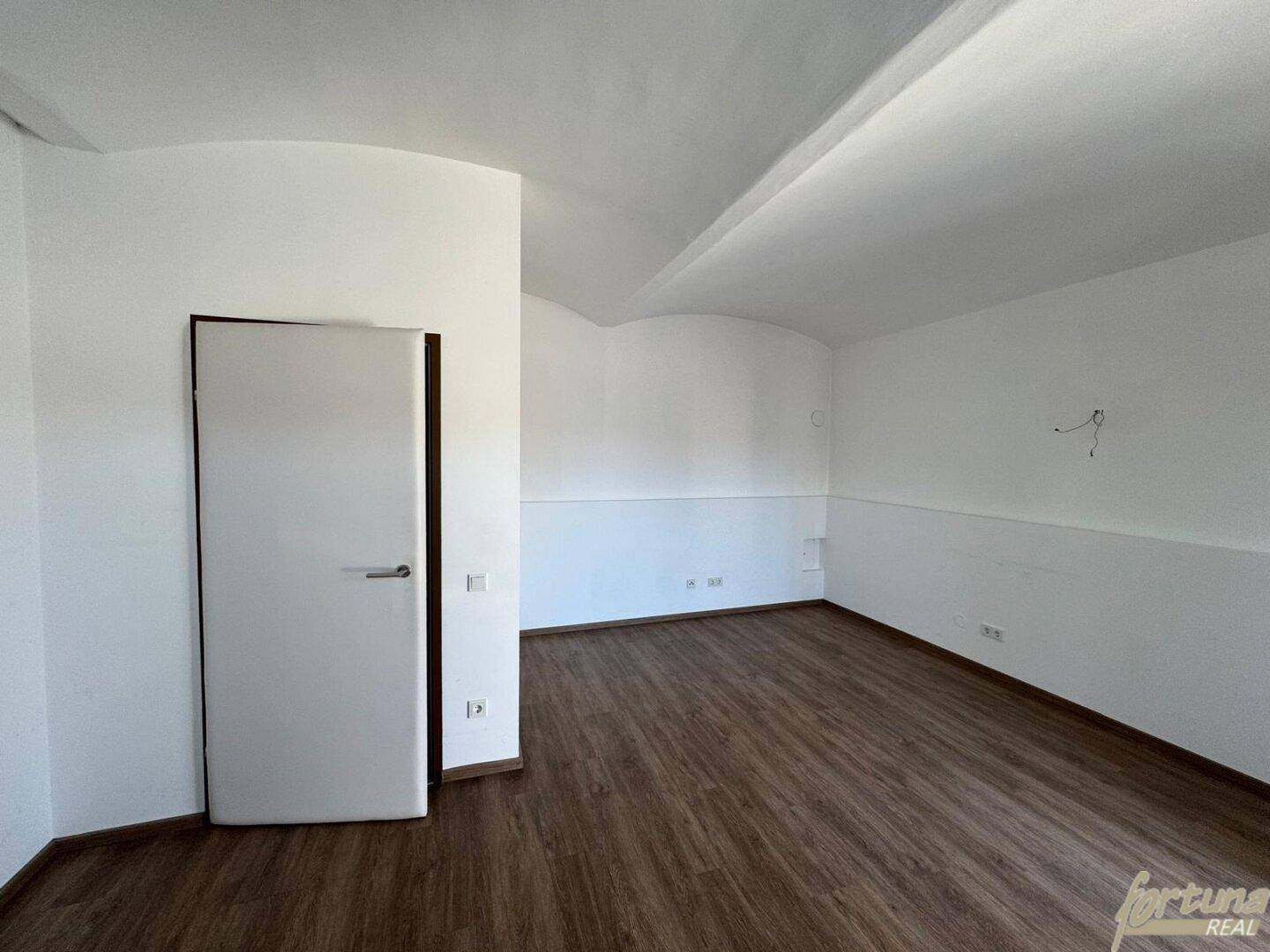 Leerer Raum mit Laminatboden, weißen Wänden und einer modernen Innentür.